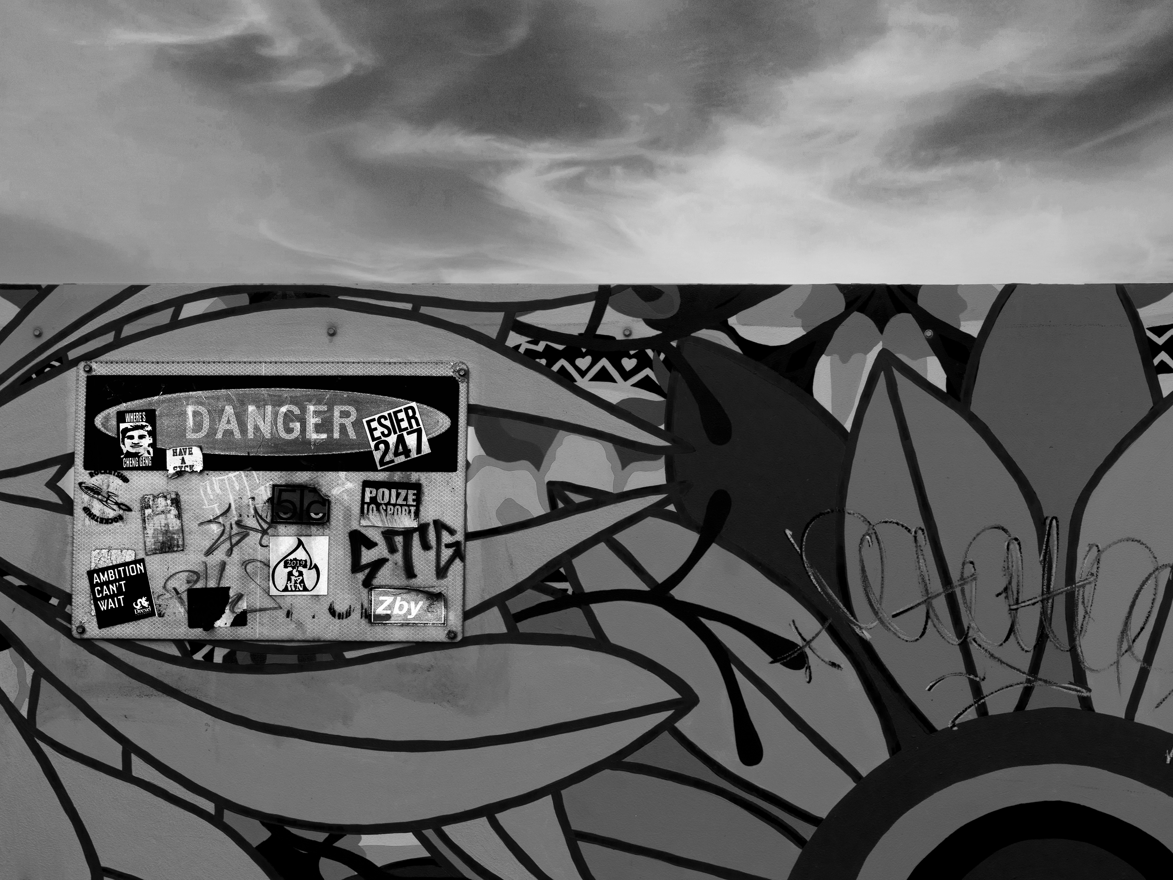 Black and white image of graffitied side of highway with a "DANGER" sign.