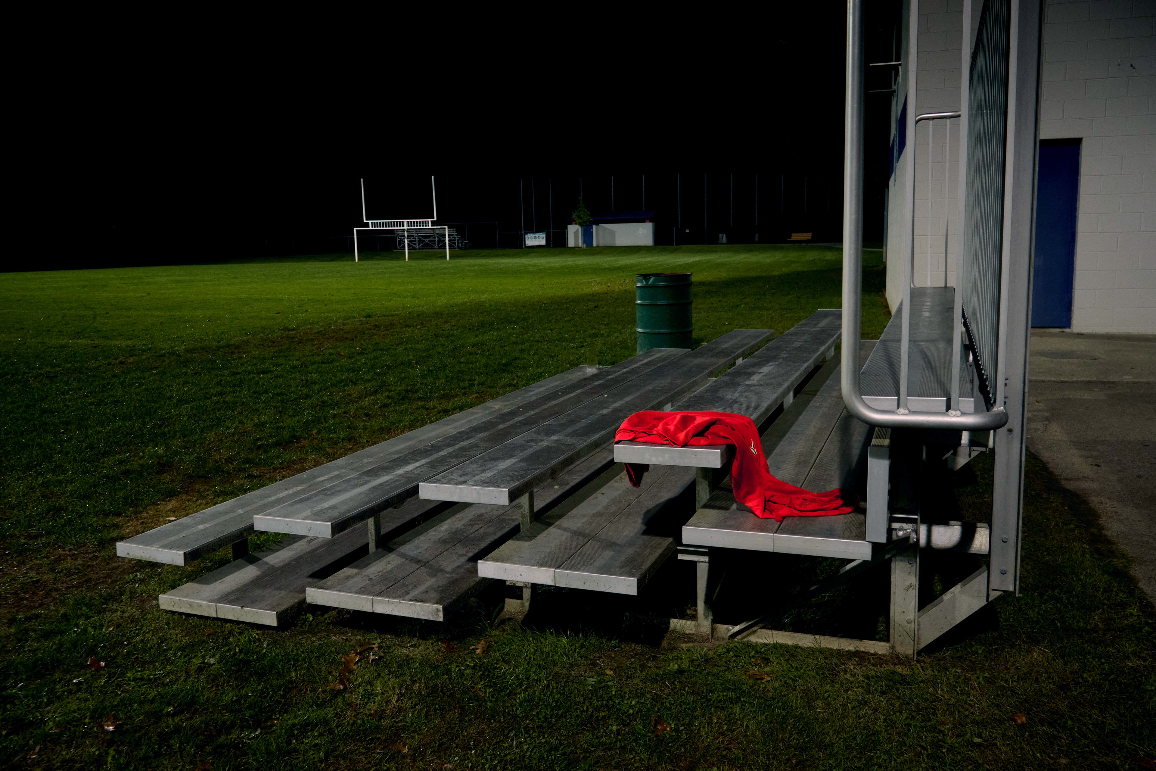 Bleachers on the side of a football field with a red sweatshirt drooped on one of the benches.