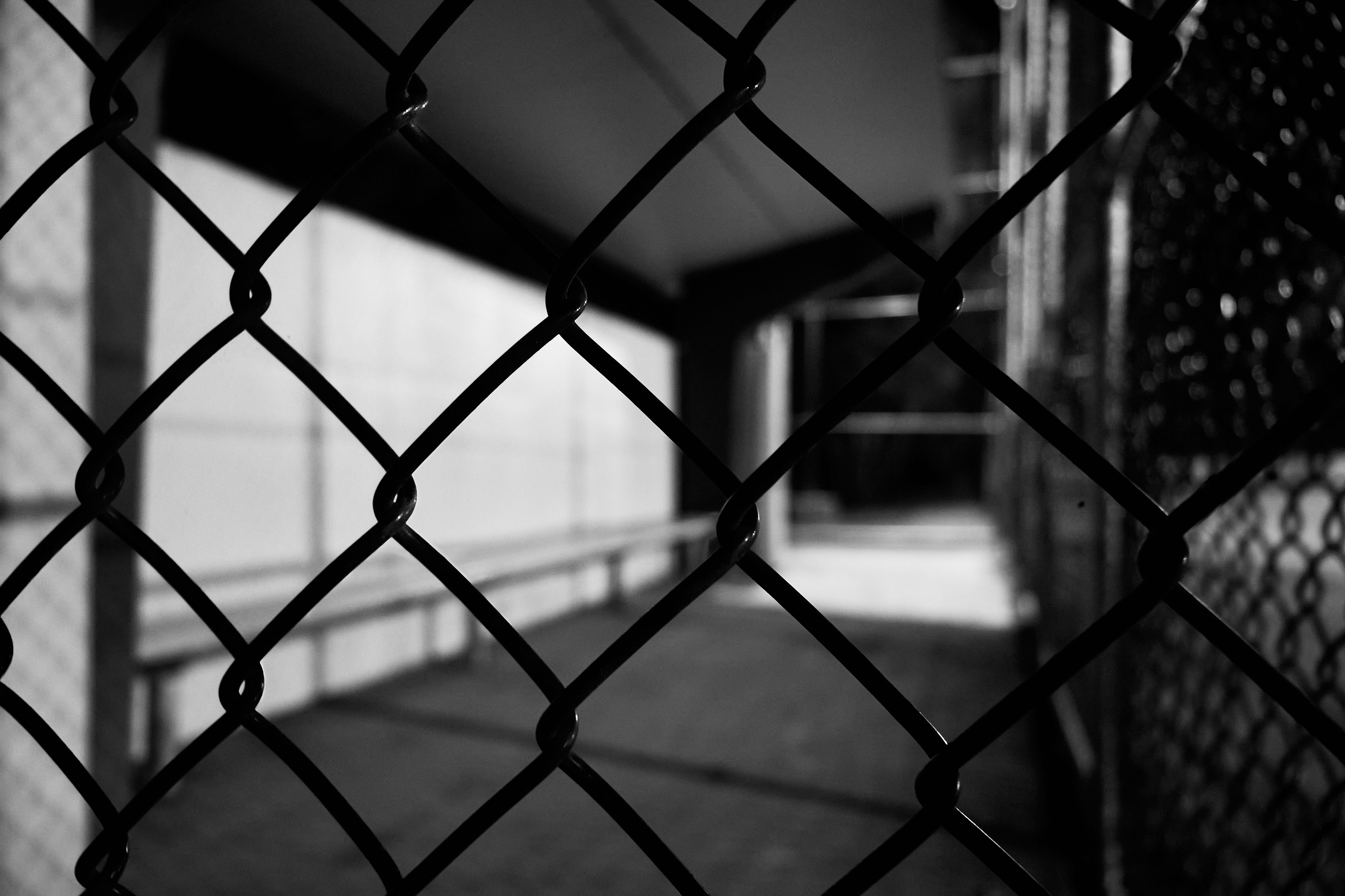 Black and white image of a baseball dugout at night blurred behind fence.