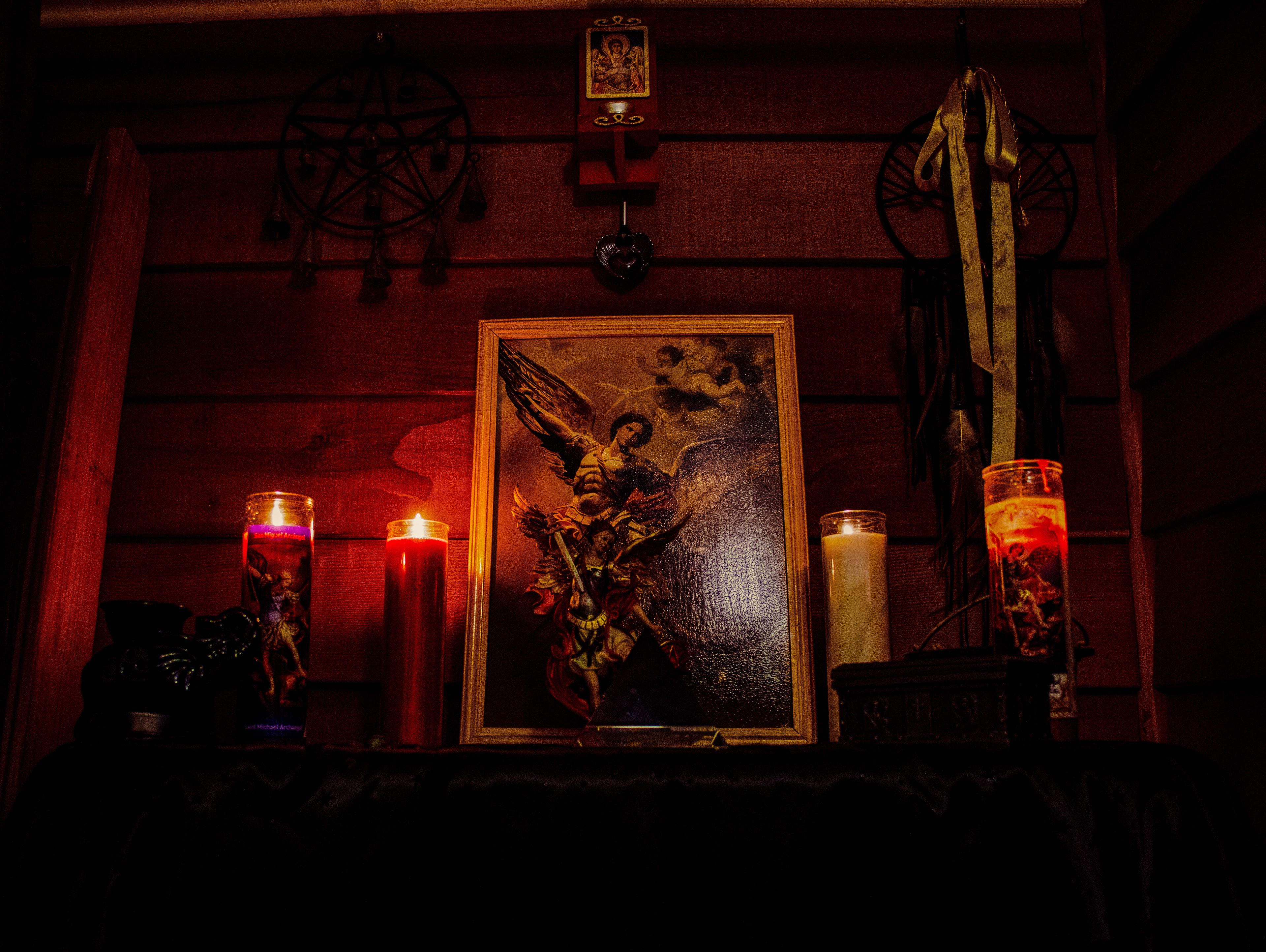 An altar in low light with a framed painting of Archangel Michael surrounded by four lit candles.