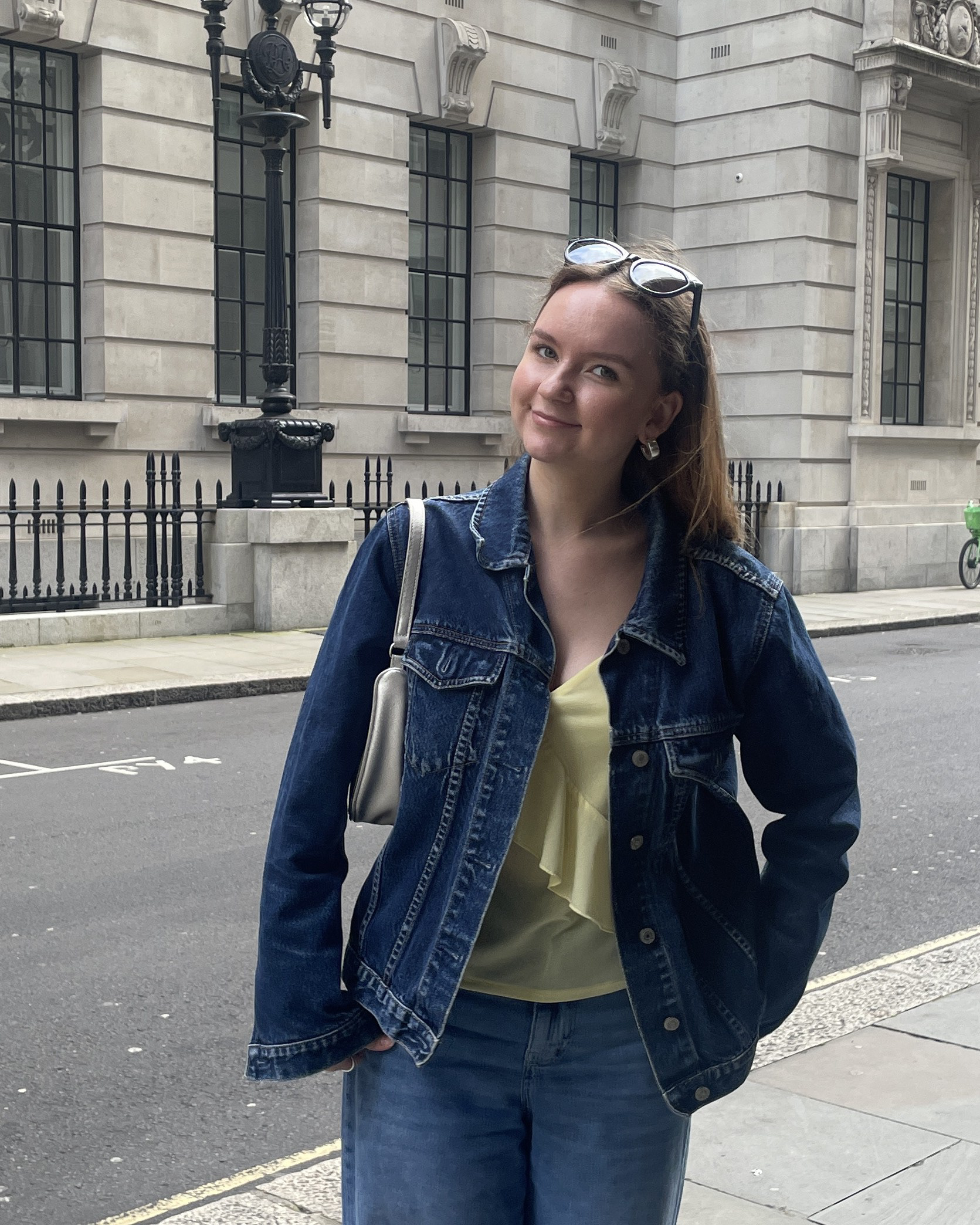Elise Meek standing in a street in London wearing a yellow frilly top, with denim jeans and jacket as well as sunglasses