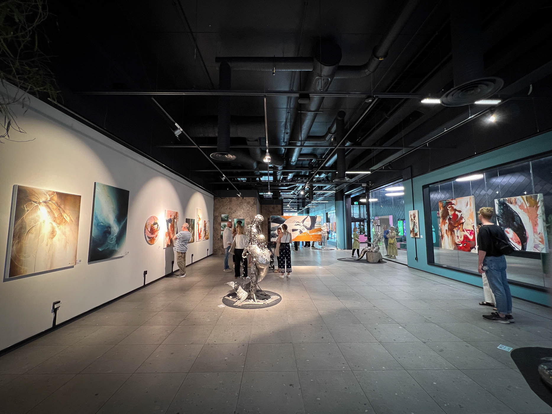 A captivating view of 'JENESAIS' art exhibition in Espoo: A vibrant pop-up gallery amidst the bustling shopping center, showcasing diverse artistic talents including Suvi Nurmi, Lotta Sirén, and Marianne Raikkala.
