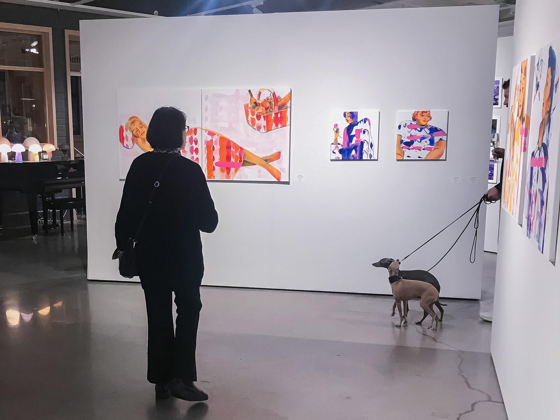Photograph capturing the joyous atmosphere at Gumbostrand Konst & Form, with dogs happily exploring Elli Maanpää's colorful paintings.