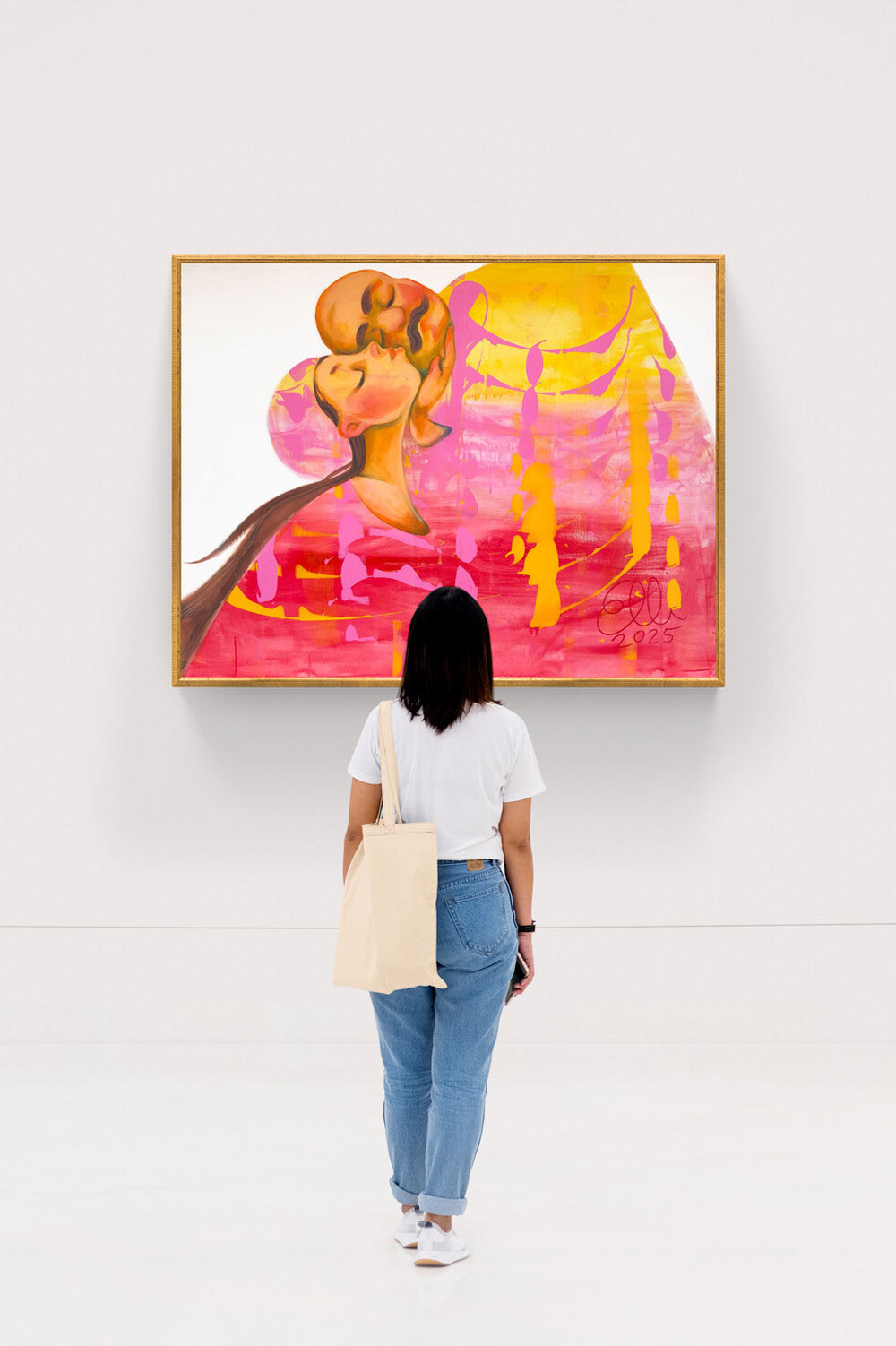 A woman stands in front of Elli Maanpää’s painting Kiss, displayed on a large white gallery wall. The artwork features two abstracted figures in a warm, layered palette of pink, orange, and yellow, sharing a tender embrace.