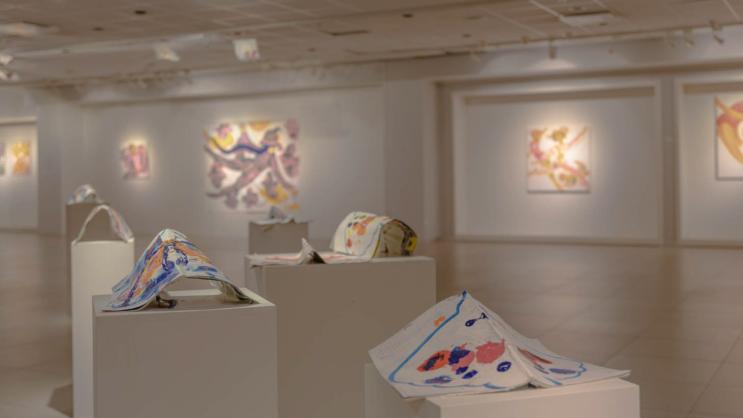 A close-up view of the site-specific installation made from magazines, with Elli Maanpää's vibrant acrylic paintings visible in the background of the light-filled gallery space. Photograph by Iiris Hellsten.
