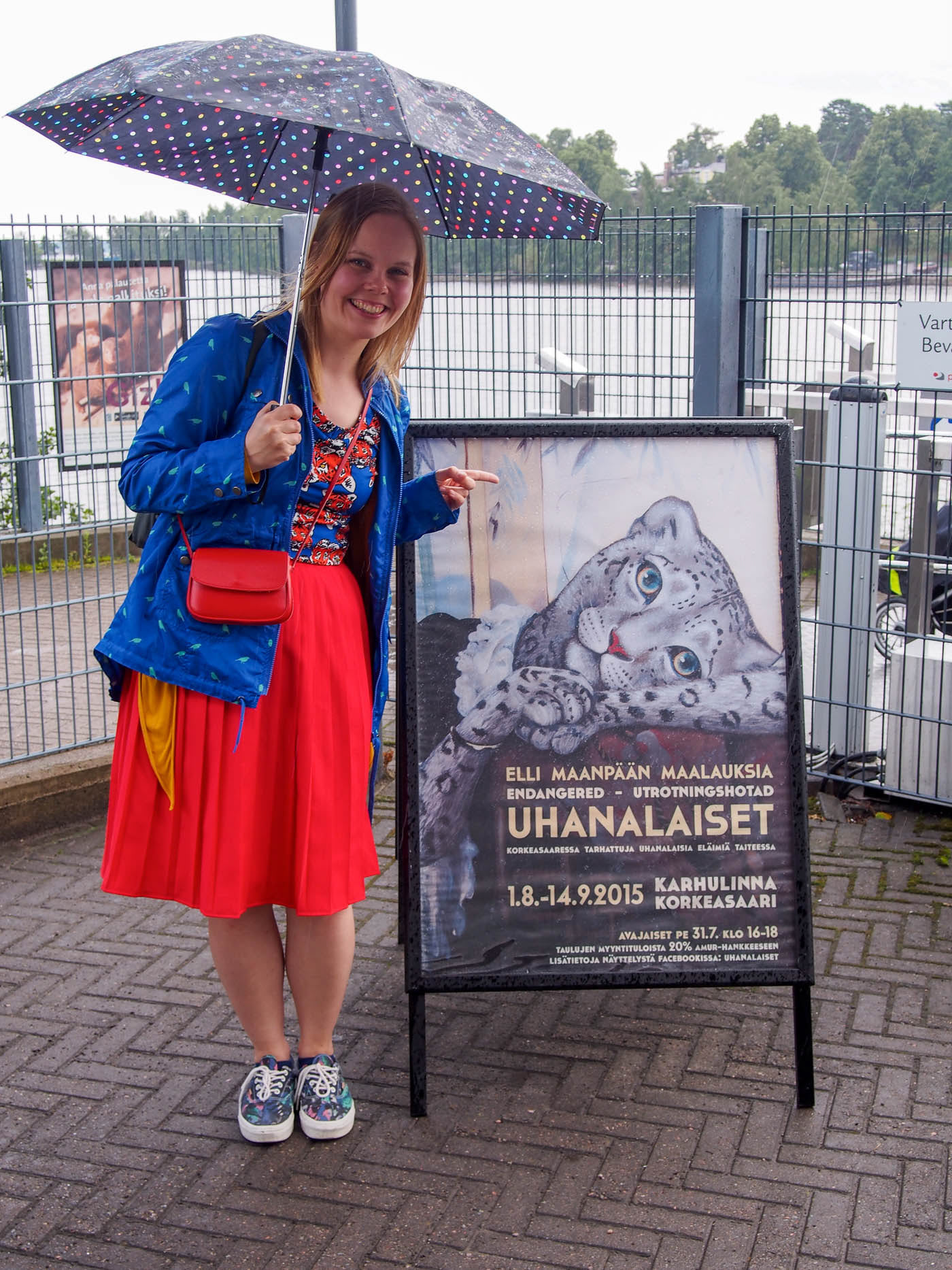 Artist Elli Maanpää posing next to the Uhanalaiset exhibition poster at Helsinki Zoo.