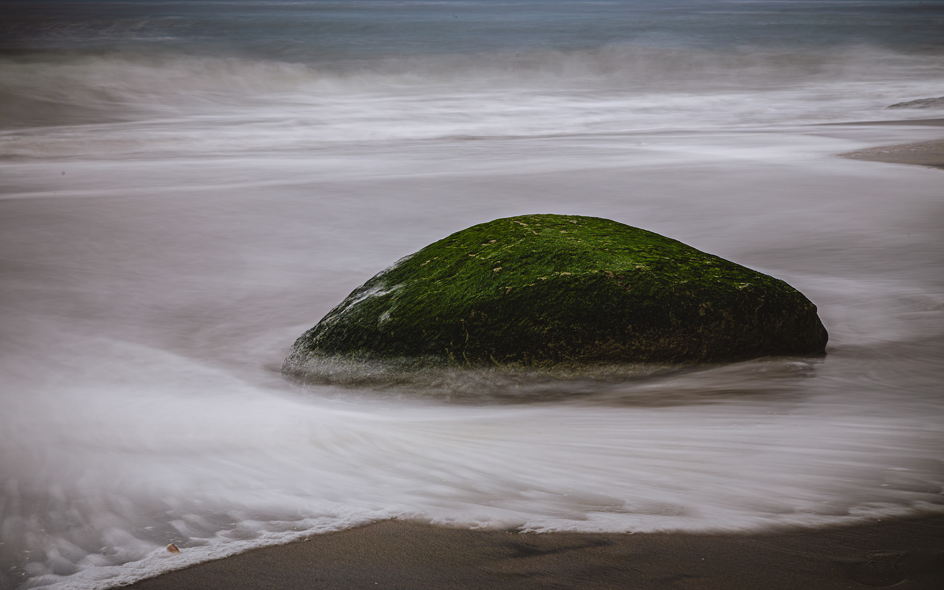 long exposure of the waves on the beach around a mossy rock