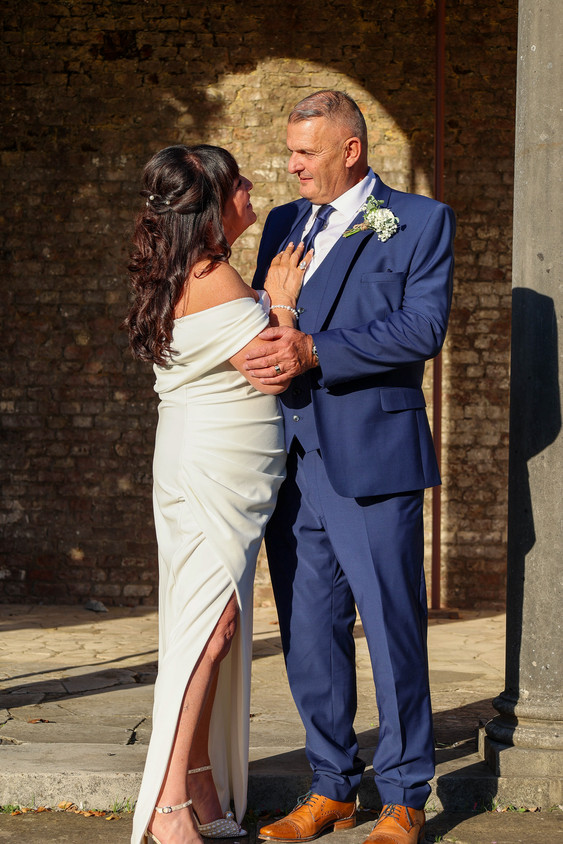 Newlyweds share a sunlit embrace beneath a floral wedding arch in Canterbury, Kent.