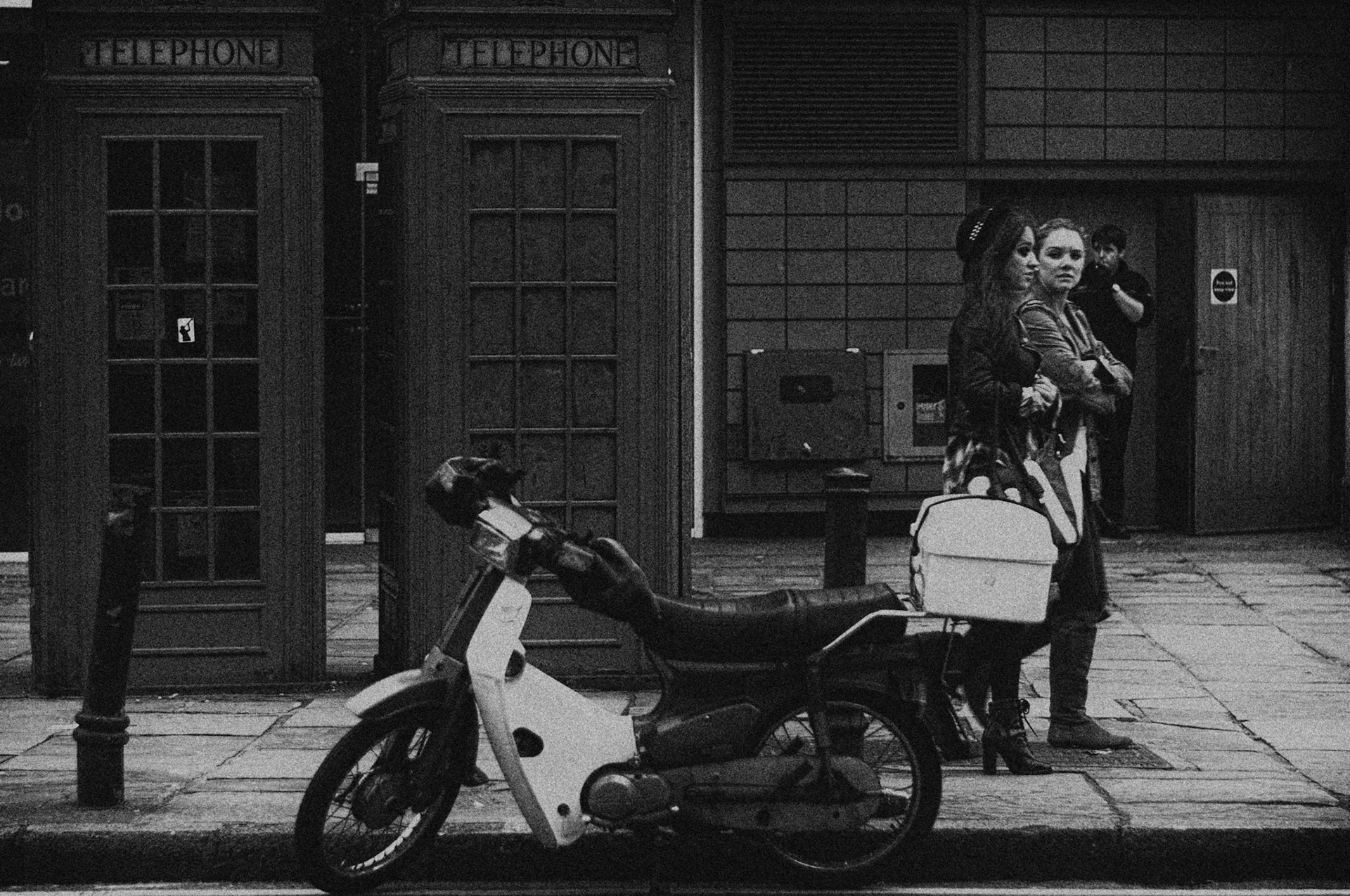 These two girls are walking straight past the old-fashioned telephone boxes and moped, leaving the era of black and white and making their way back to colour.