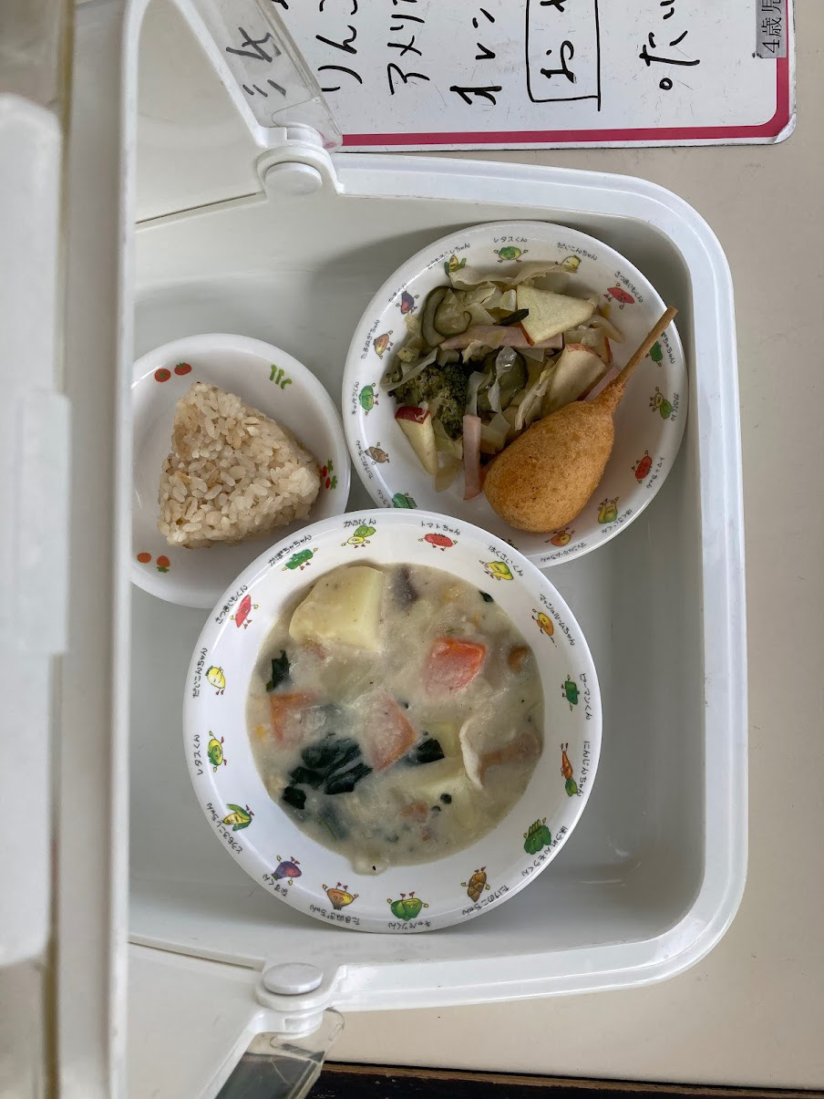cream stew, corn dog, cucumber potato salad with a onigiri snack