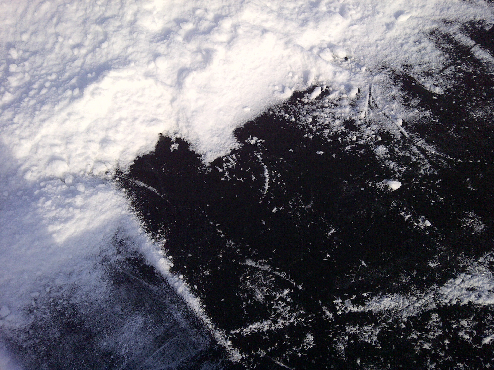 Pikzwart ijs onder de sneeuw