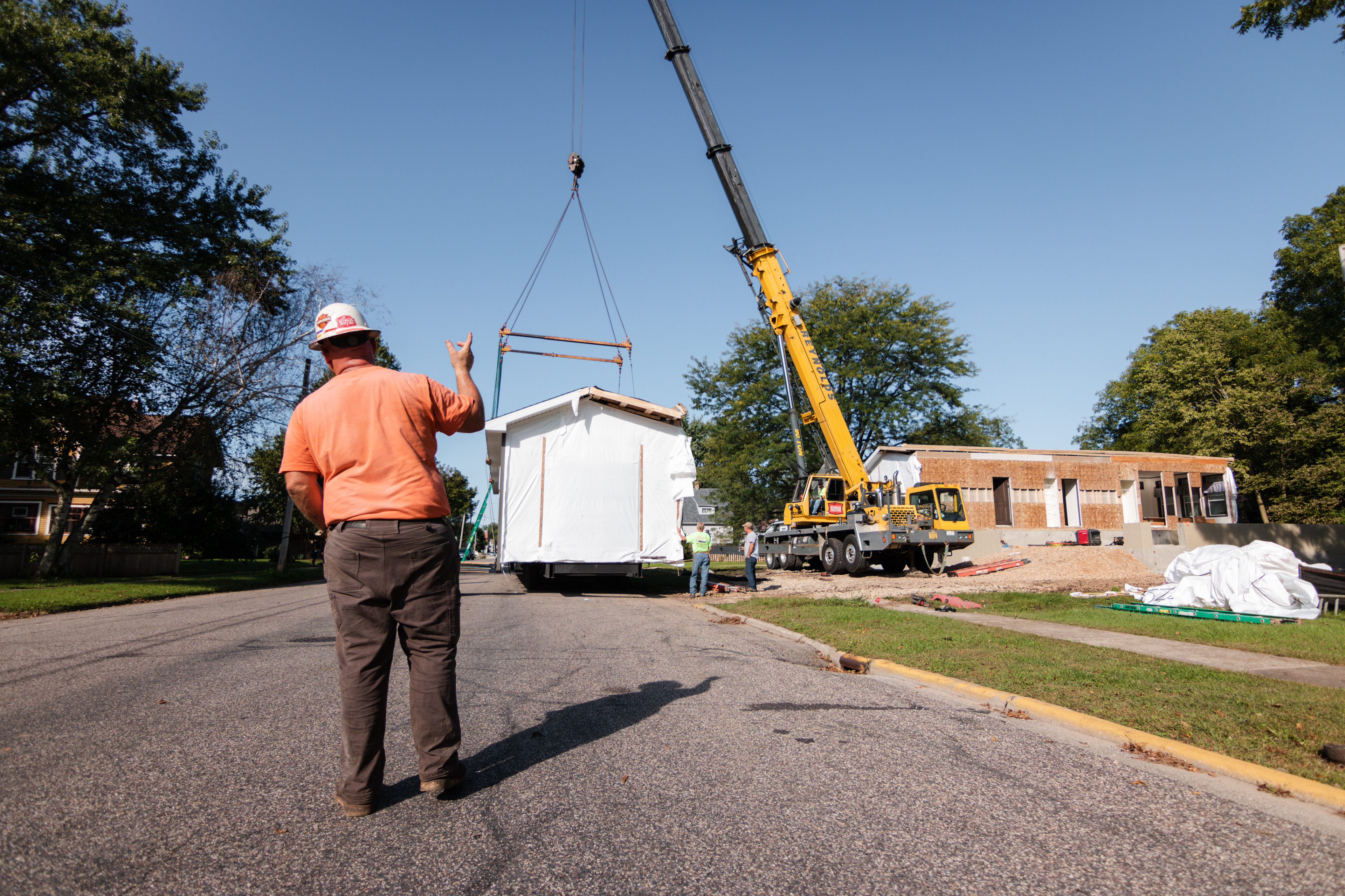 A worker directs the crane operator for lifting the home.
