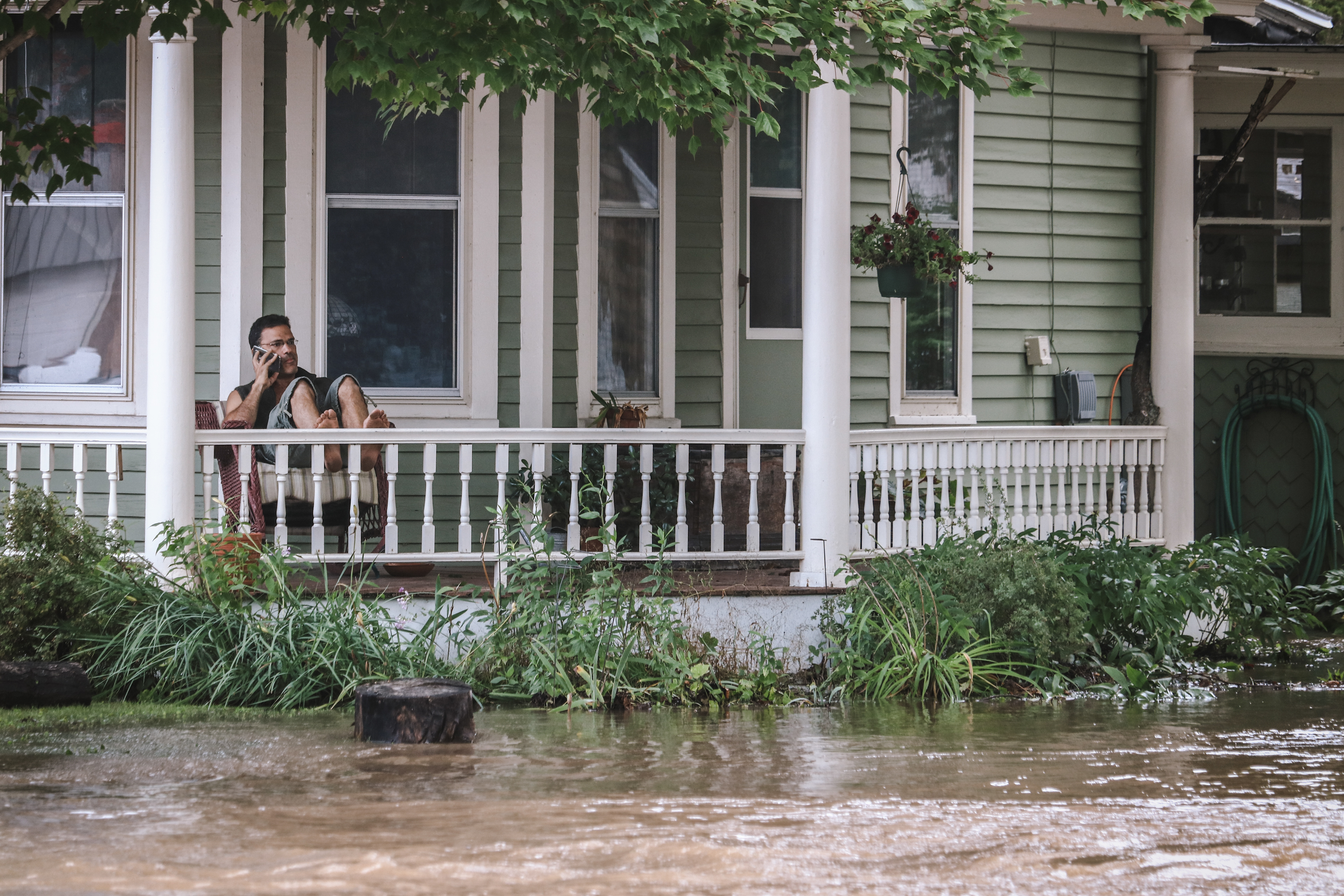 Jason Sromovsky sits on his front porch on the phone as flood waters surround his home.