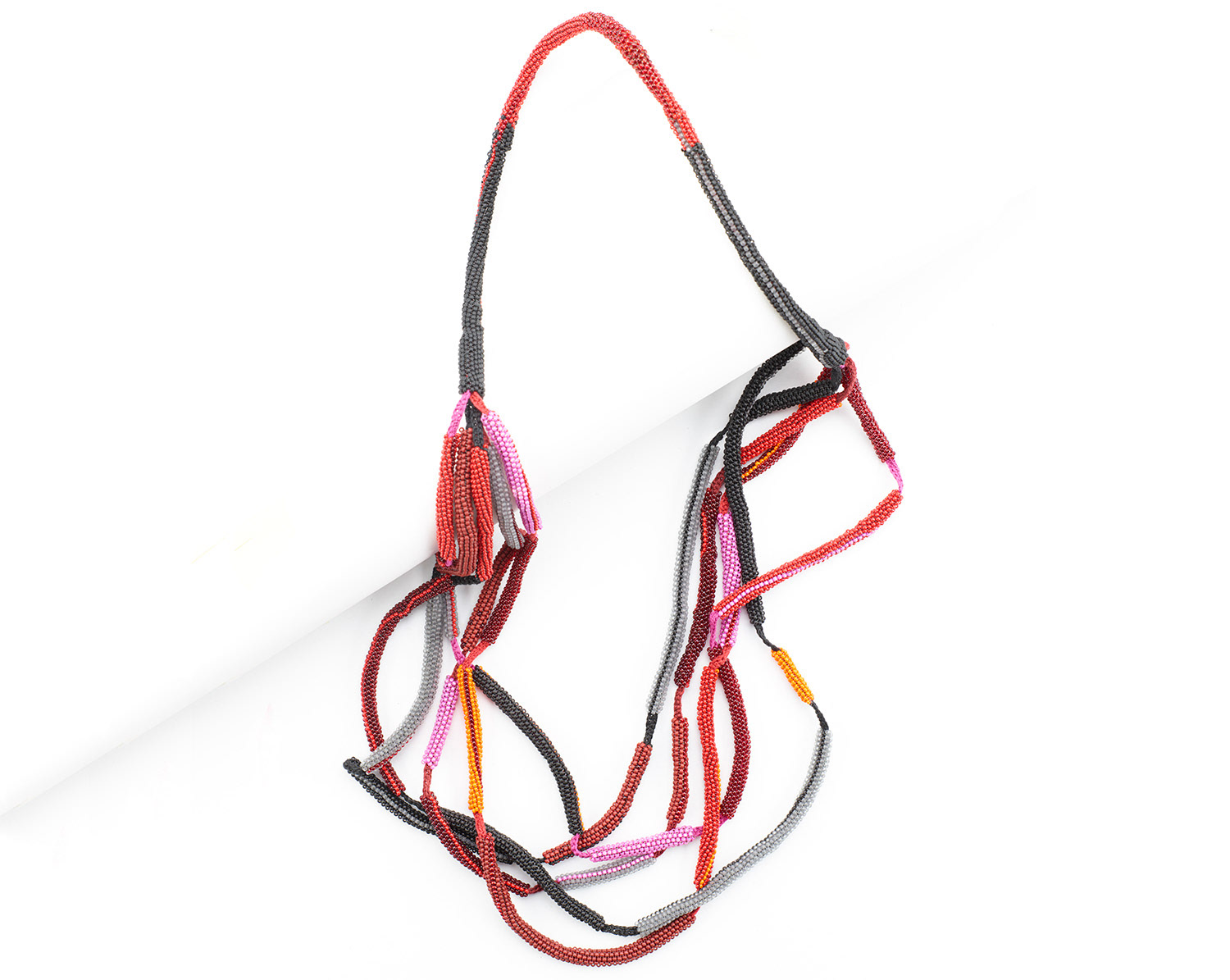 Lange Halskette, gehäkelt und teilweise mit Glasperlen umfädelt. Die Kette besteht aus fünf Strängen, die oben zu einem Strang zusammengefasst sind. Farben: Schwarz, Grau, Orange, Rot, Pink.