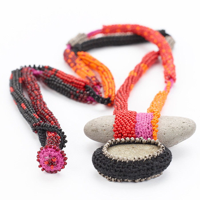 Zwei helle Kiesel mit gehäkelter Fassung aus schwarzem und Pinkfarbenem Garn an langer Häkelkette, mit Glasperlen in Schwarz, Rot, Pink und Orange umfallet.