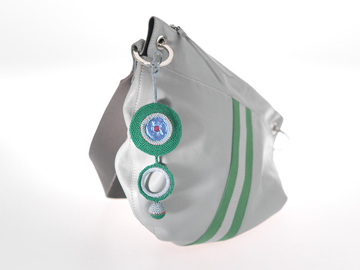 Gehäkelter Taschenschmuck in Grün und Grau, aus zwei runden Elementen und unten einer Kugel. Das obere Element besteht aus einer in runden umhäkelten Kaffeekapsel, die flachgehämmert wurde.