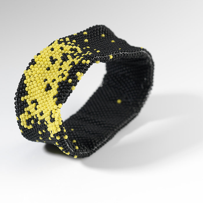Armband aus matten schwarzen und hellgelben Perlen gefädelt. Das Muster erinnert an die Lichter einer Stadt bei Nacht aus dem Flugzeug beobachtet.