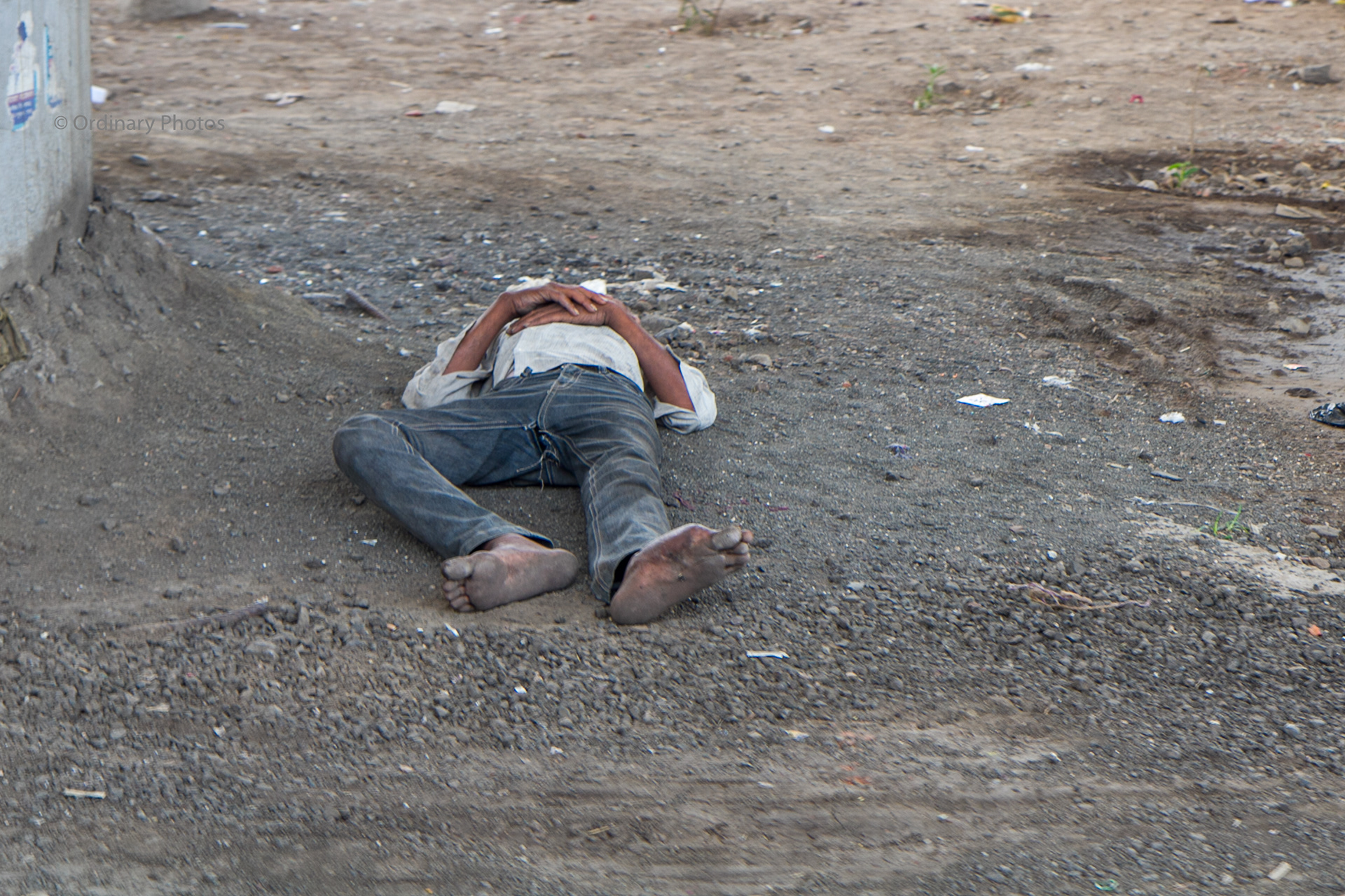 A man sleeping on the gravel under a bridge in Nashik