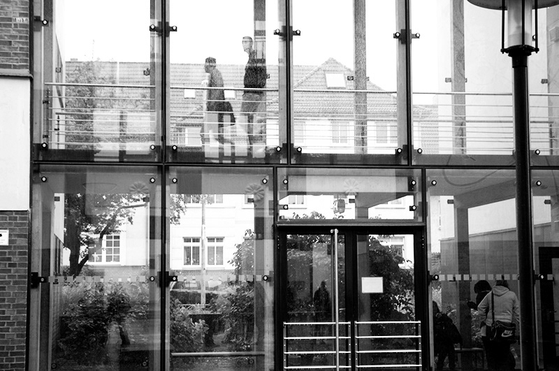 glasfassade einer schule, schwarz-weiß. oben laufen menschen. außenaufnahme