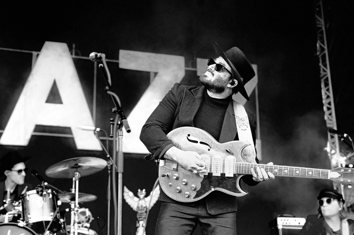 sw Foto des Sängers Angus Stone. Er schaut auf der Bühne eine Gitarre haltend nach oben. Singer Angus Stone on Stage with a guitar. Black and white picture of Angus Stone