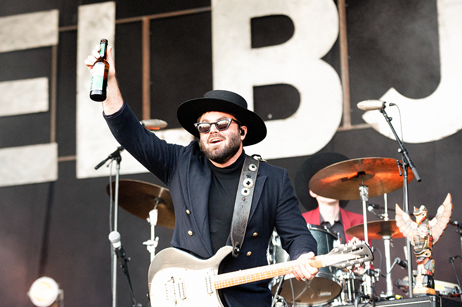 angus stone on stage, smilog and holding a bottle of beer