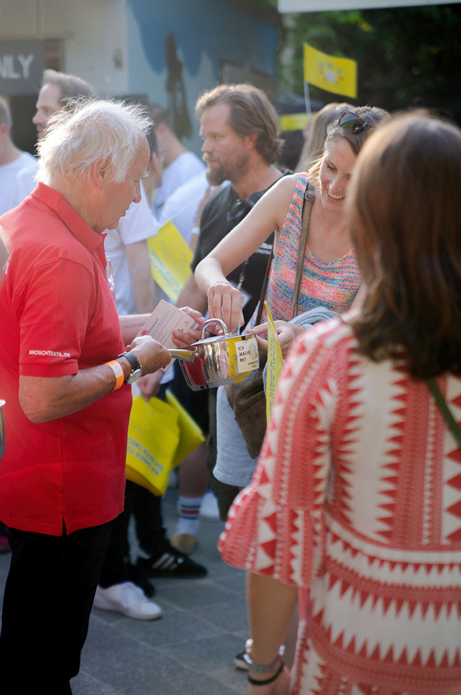a man collecting money. a smiling woman is donating. its sunny and outdoor