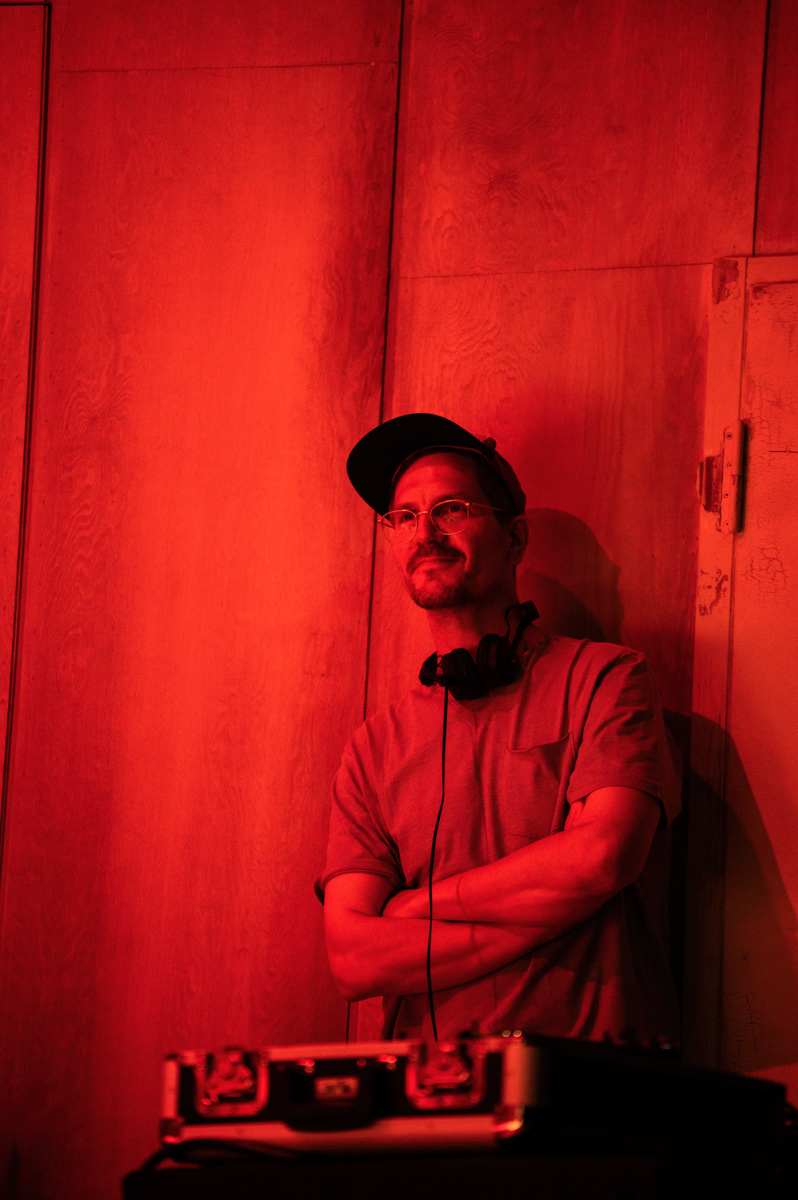 dj lehnt an einer wand und lächelt. das foto ist in rotem licht