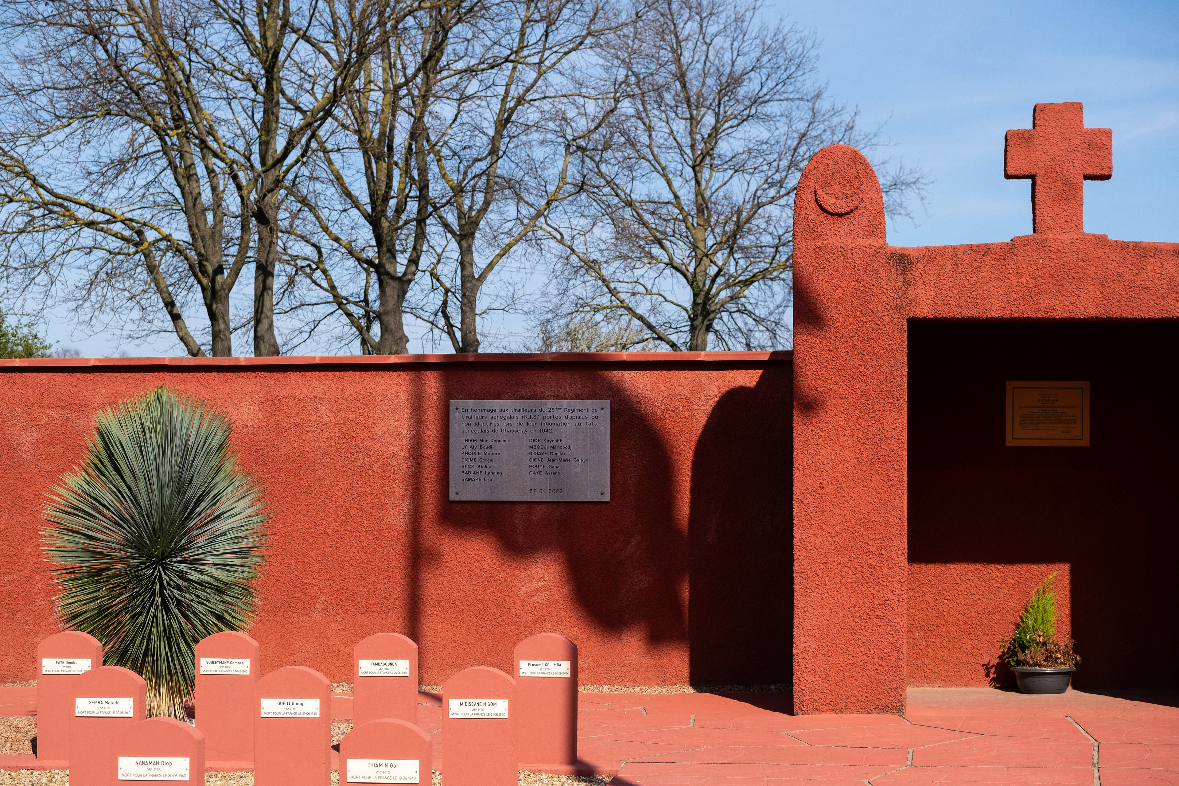 Entrée avec murs rouges distinctifs et drapeau français flottant. Hommage aux tirailleurs sénégalais de la Seconde Guerre mondiale. Patrimoine mémoriel et attrait touristique. Photo par Etienne Gatheron, spécialiste des sites historiques, patrimoine culturel et tourisme mémoriel.