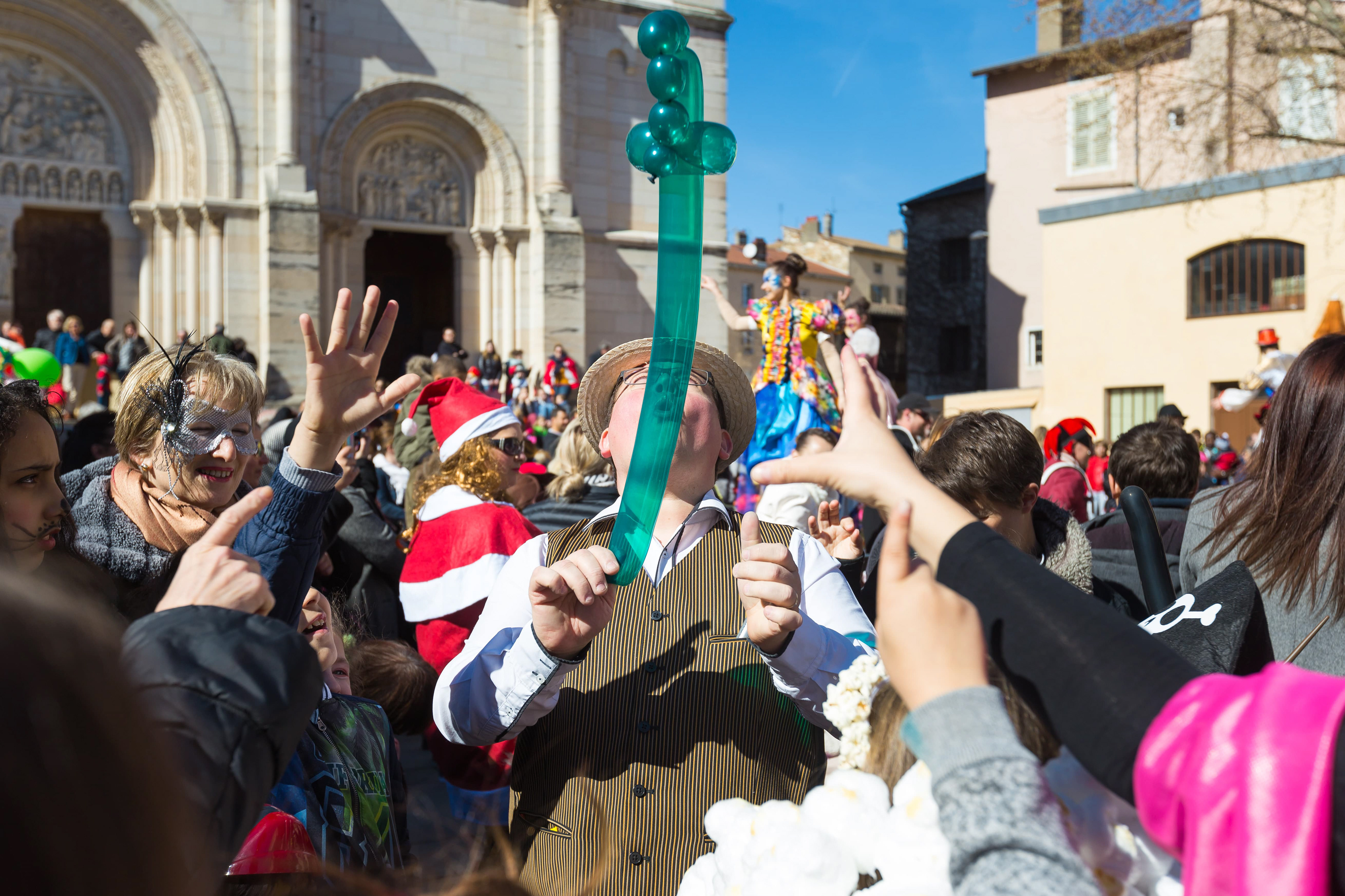 Scène animée d'un carnaval à Mâcon, Saône-et-Loire, Bourgogne, Rhône-Alpes, avec un artiste de rue distribuant des ballons sculptés et une foule de participants costumés, sous un ciel ensoleillé. Photographie capturée par Etienne Gatheron. Photographie institutionnelle.