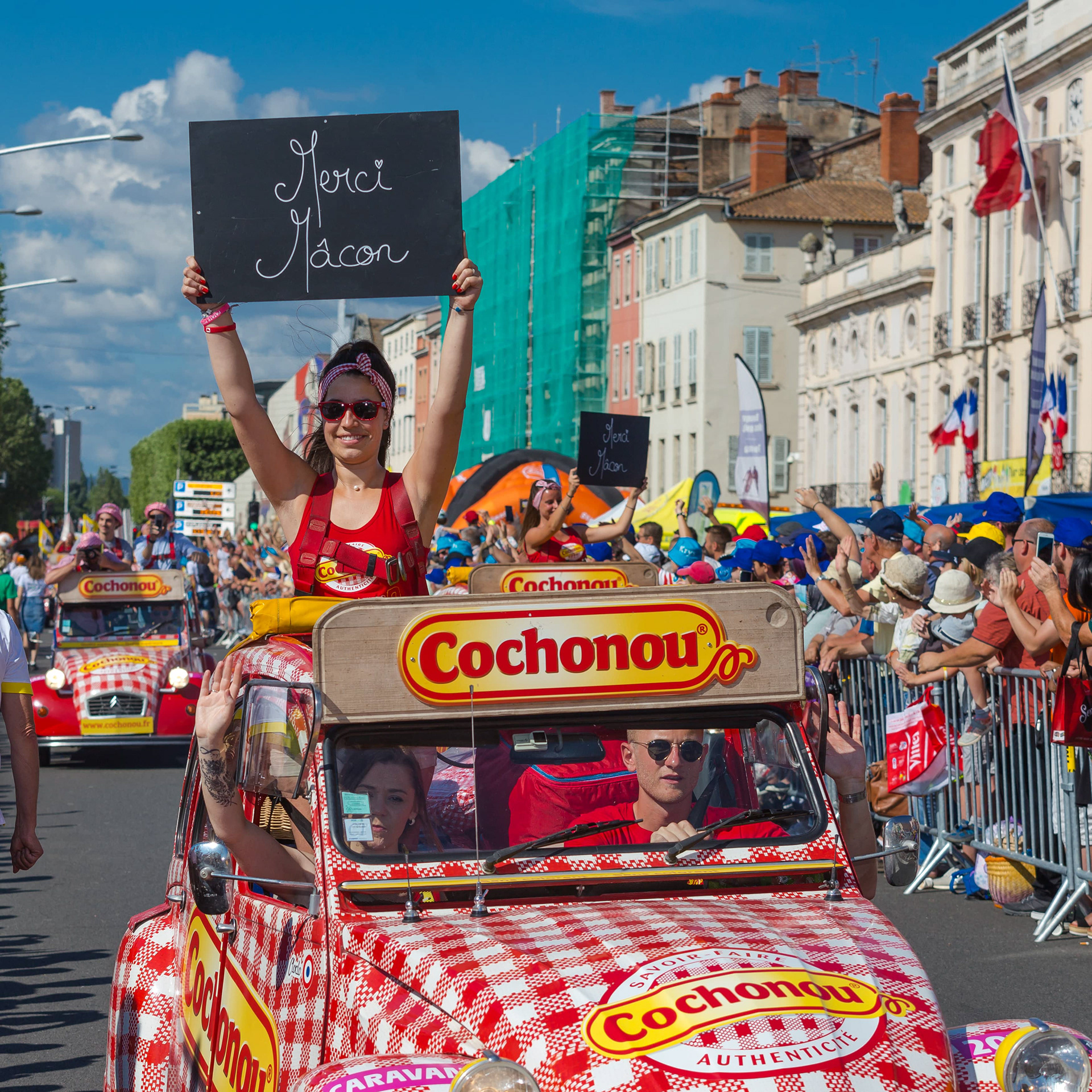Caravane Cochonou lors du Tour de France à Mâcon, Saône-et-Loire, Bourgogne, Rhône-Alpes, avec des animateurs saluant la foule et des voitures décorées. Photographie capturée par Etienne Gatheron. Photographie institutionnelle.