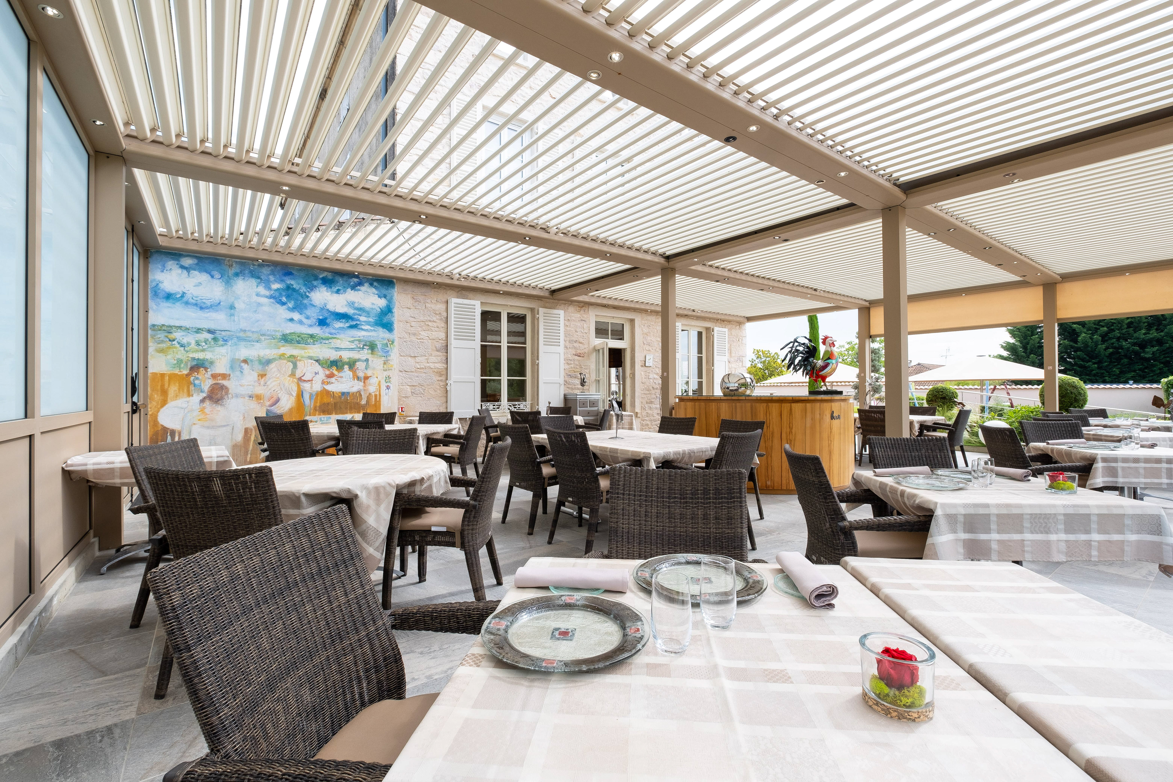Terrasse de La Marande à Montbellet en Saône-et-Loire, Bourgogne, avec des tables élégamment dressées sous une pergola moderne, offrant une décoration artistique et une ambiance accueillante pour un repas en plein air, mettant en valeur la qualité et le charme de l'établissement.
