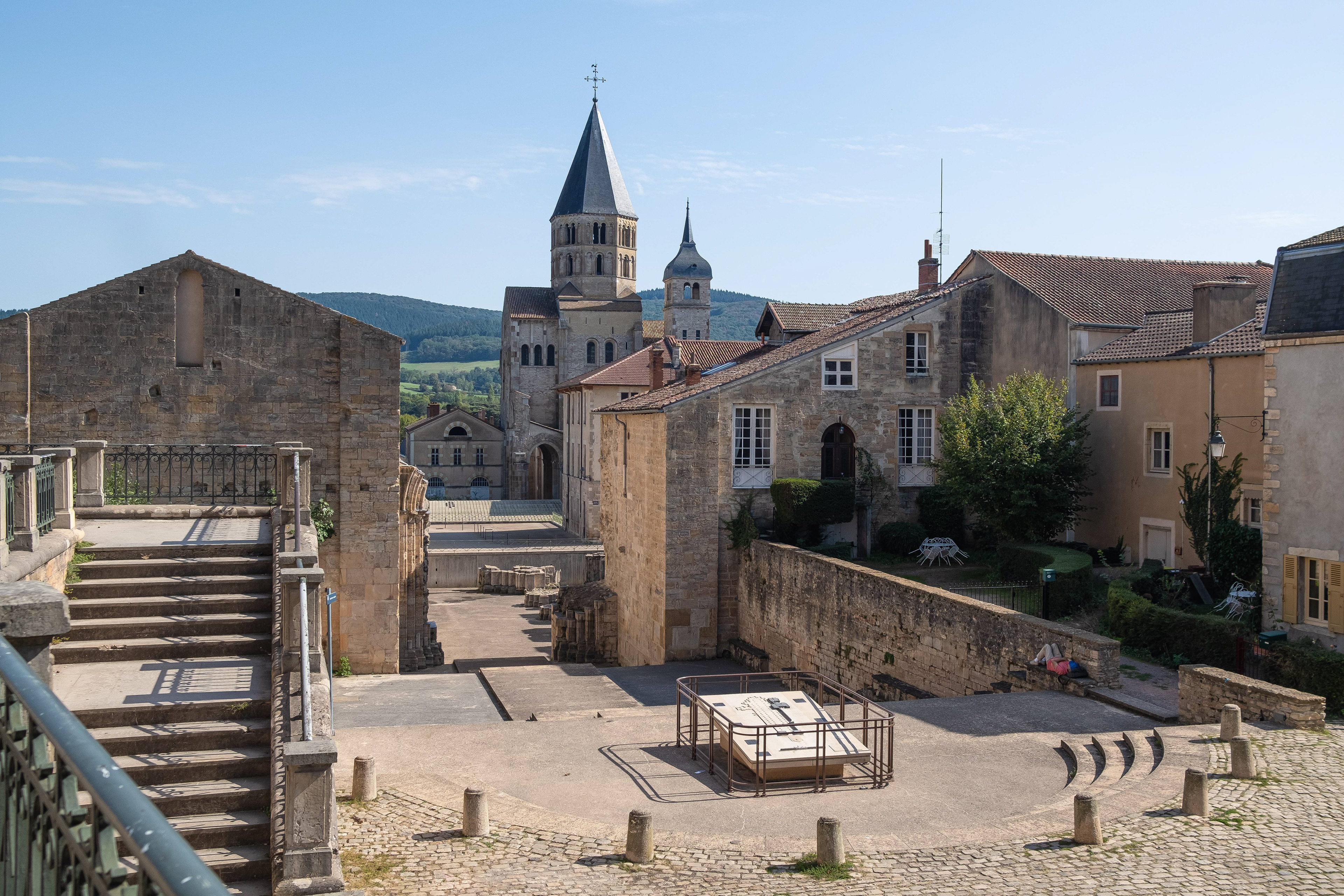 Ruines anciennes et murs historiques de l'Abbaye de Cluny sous un ciel bleu clair, avec clocher d'église et bâtiments en pierre bien conservés. Importance culturelle et religieuse de Saône-et-Loire, Bourgogne. Photographie touristique par Etienne Gatheron, expert en sites historiques et patrimoine culturel.