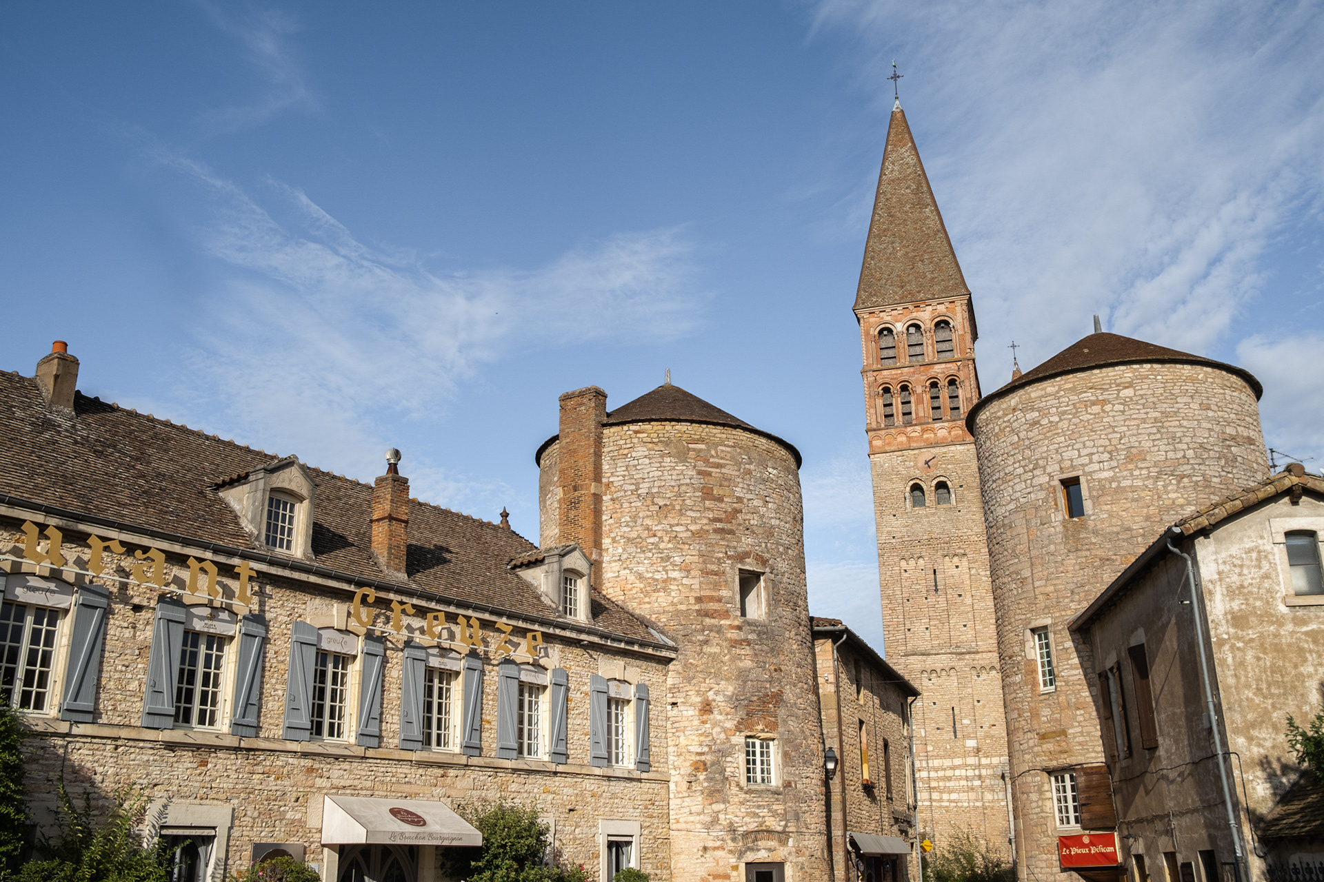 Clocher et tours de l'Abbaye de Tournus avec bâtiments historiques adjacents sous ciel bleu. Architecture en pierre et toits en tuiles. Patrimoine culturel et attrait touristique de Saône-et-Loire, Bourgogne. Photographie touristique par Etienne Gatheron.