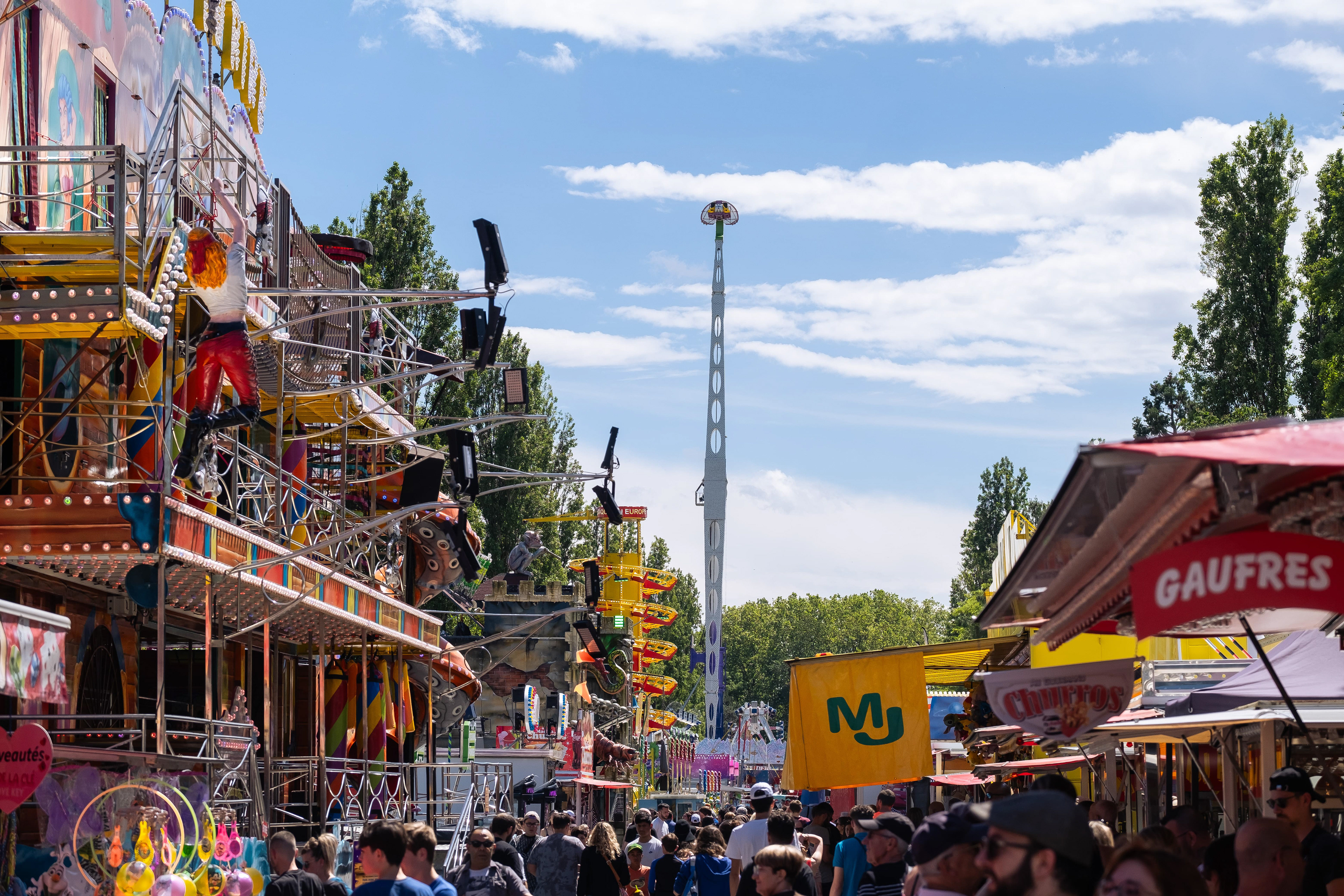 Fête foraine animée à Mâcon, Saône-et-Loire, Bourgogne, Rhône-Alpes, avec des manèges colorés, des stands de nourriture et une foule de visiteurs profitant des attractions sous un ciel bleu. Photographie capturée par Etienne Gatheron. Photographie institutionnelle.