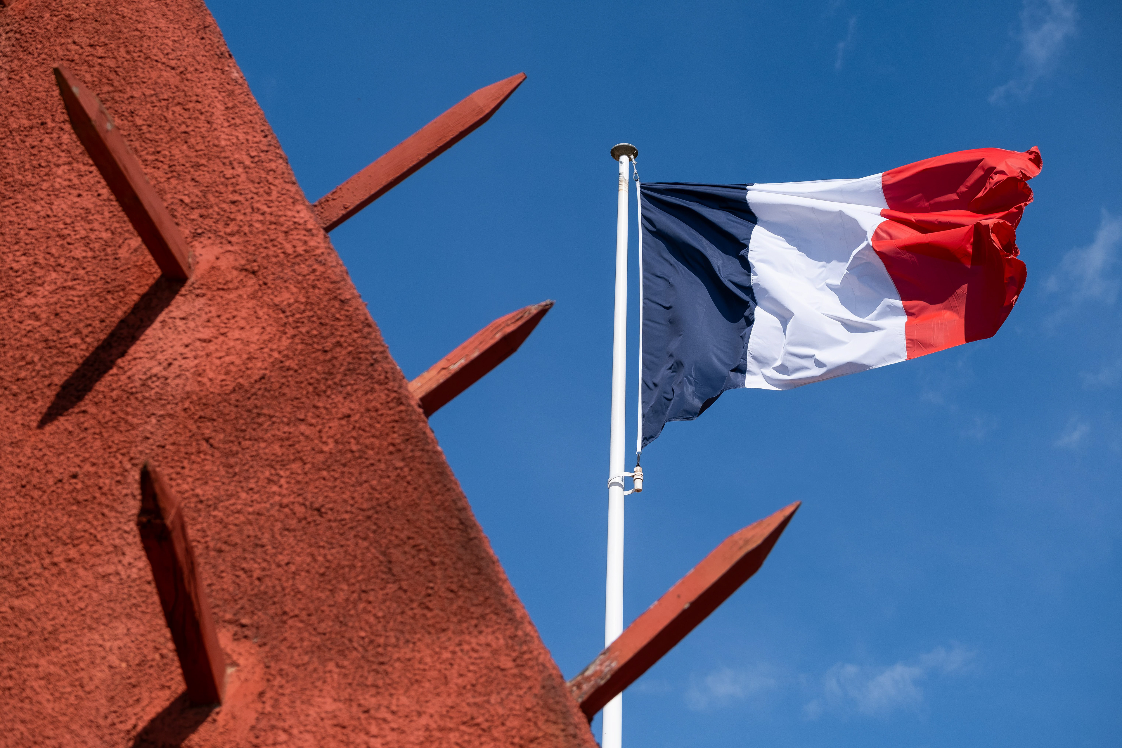 Drapeau français au-dessus du mur rouge du mémorial à Chasselay, contrastant avec le ciel bleu. Importance historique et mémorielle. Photo par Etienne Gatheron, spécialiste des sites historiques, patrimoine culturel et tourisme mémoriel.