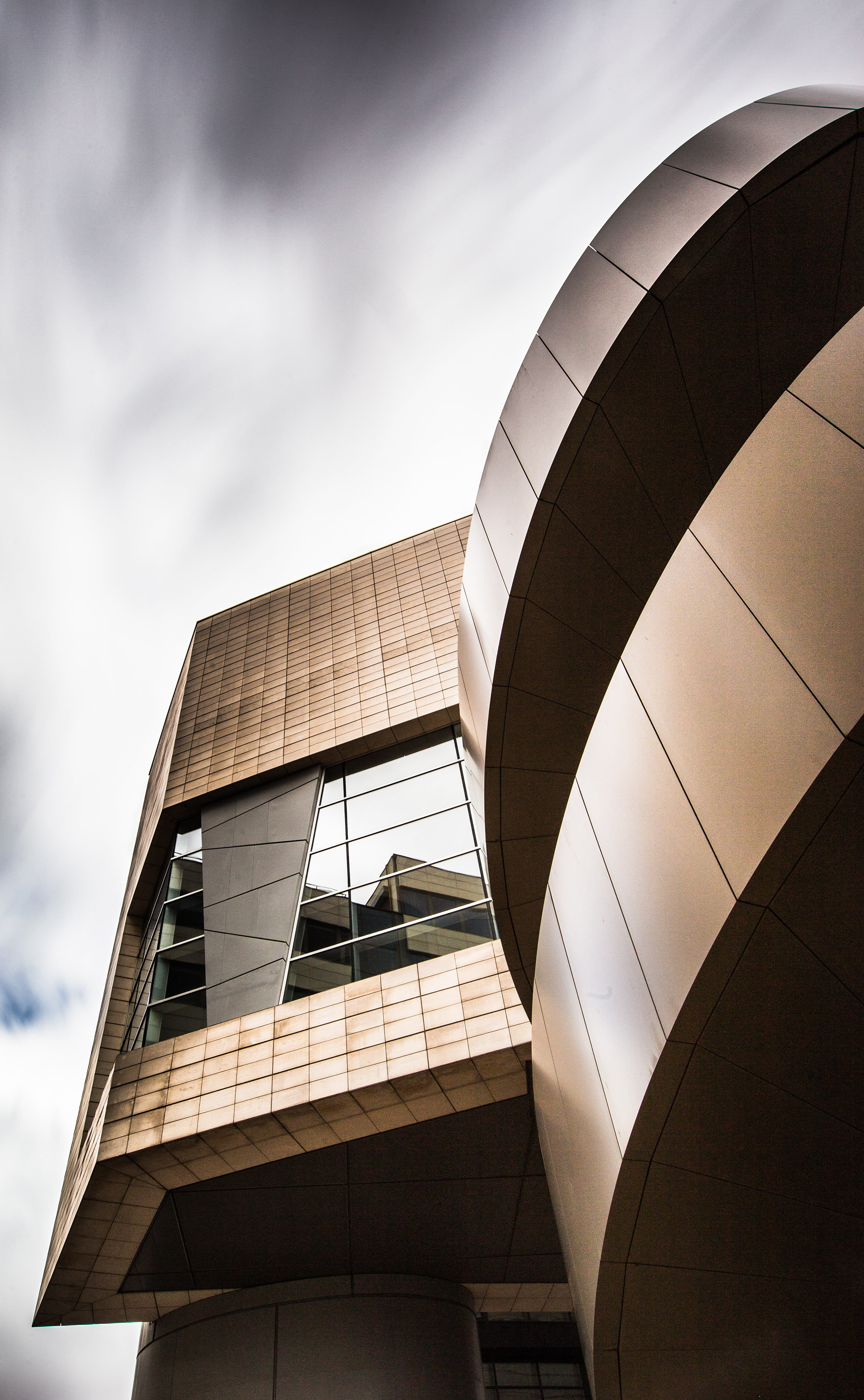 Vue architecturale de l'auditorium de Dijon : Lignes courbes et angulaires du bâtiment en métal et en verre, avec des fenêtres offrant un aperçu de l'intérieur. Photographie par Etienne Gatheron, spécialiste en architecture.