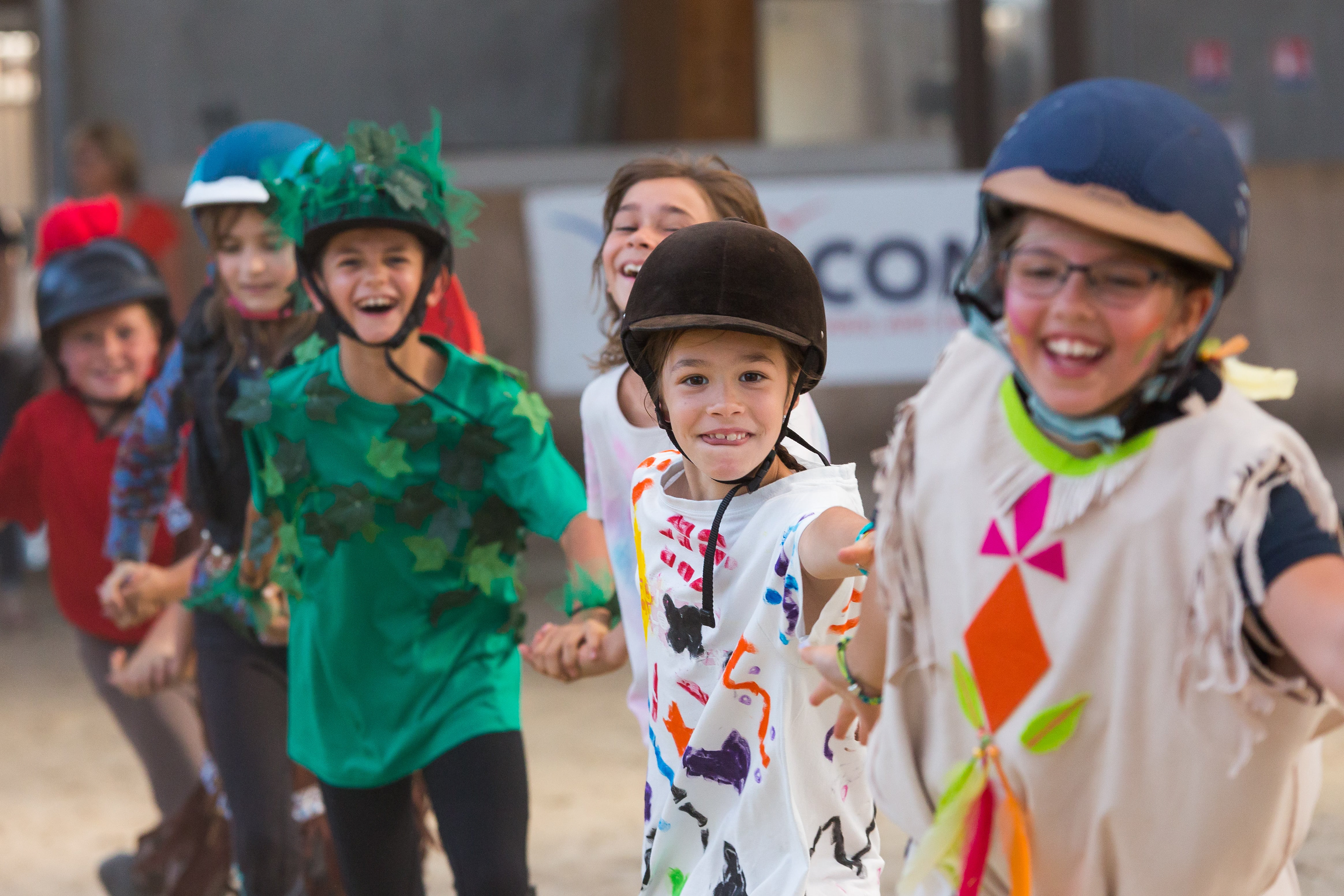 Enfants en costumes colorés et casques participant à une activité équestre, souriants et se tenant par la main dans une ambiance joyeuse à Mâcon, Saône-et-Loire, Bourgogne, Rhône-Alpes. Photographie capturée par Etienne Gatheron. Photographie institutionnelle.