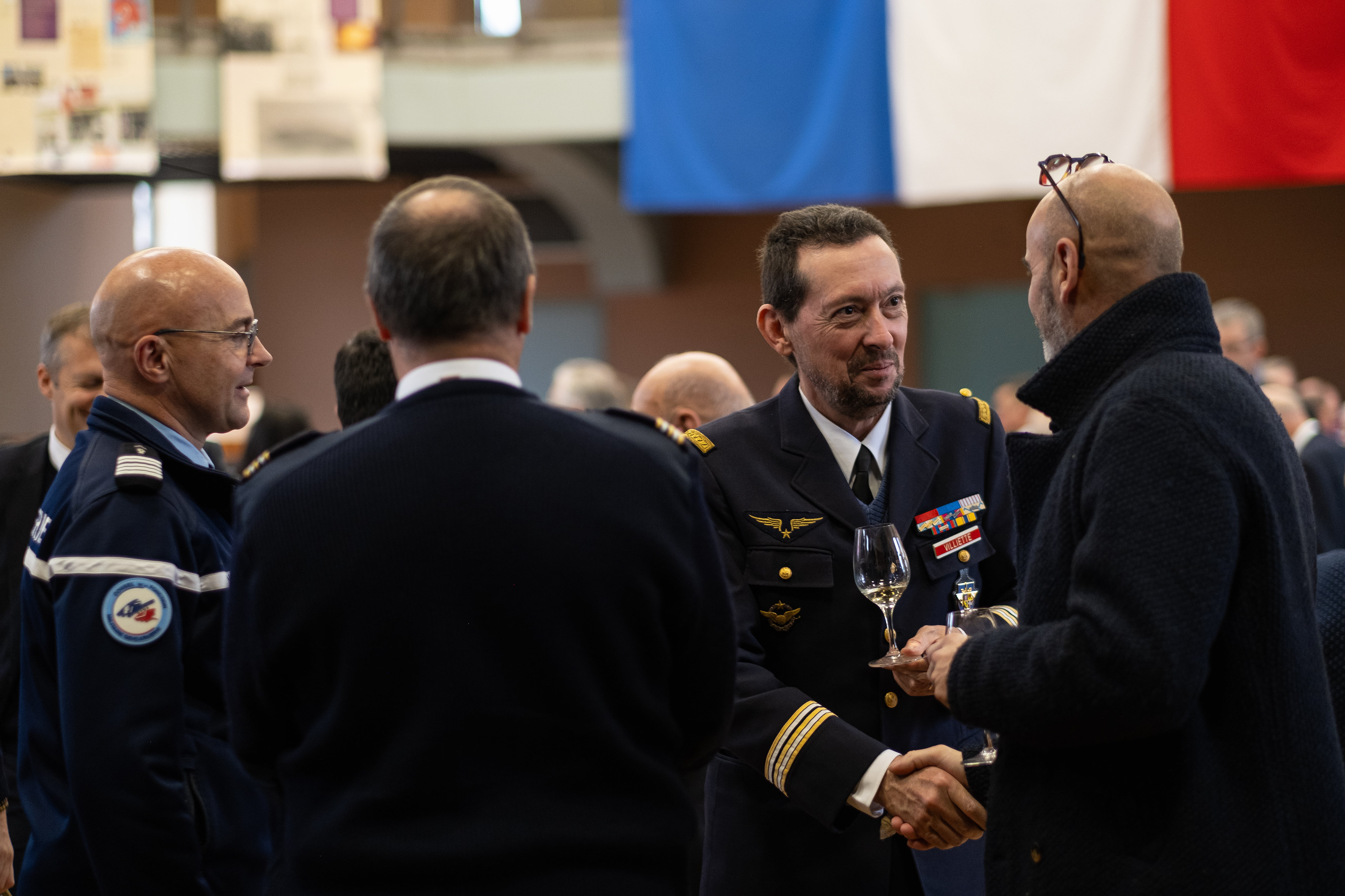 Rencontre officielle en Saône-et-Loire, Bourgogne, Rhône-Alpes avec des officiers militaires en uniforme discutant et échangeant des poignées de main lors d'un événement. En arrière-plan, des drapeaux français sont visibles, ajoutant une touche patriotique à la scène. Photographie capturée par Etienne Gatheron. Photographie institutionnelle.