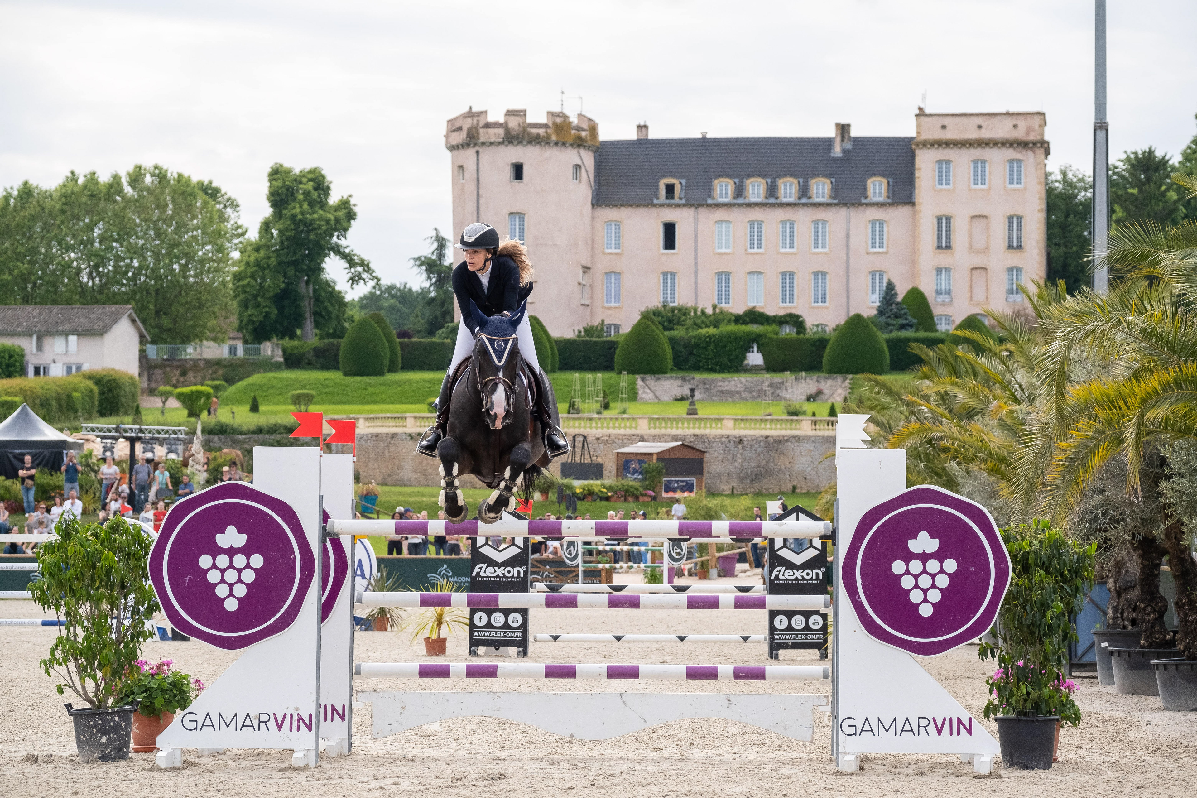 Cavalier participant à un concours de saut d'obstacles à Mâcon, Saône-et-Loire, Bourgogne, Rhône-Alpes, avec un château en arrière-plan. Photographie capturée par Etienne Gatheron. Photographie institutionnelle.