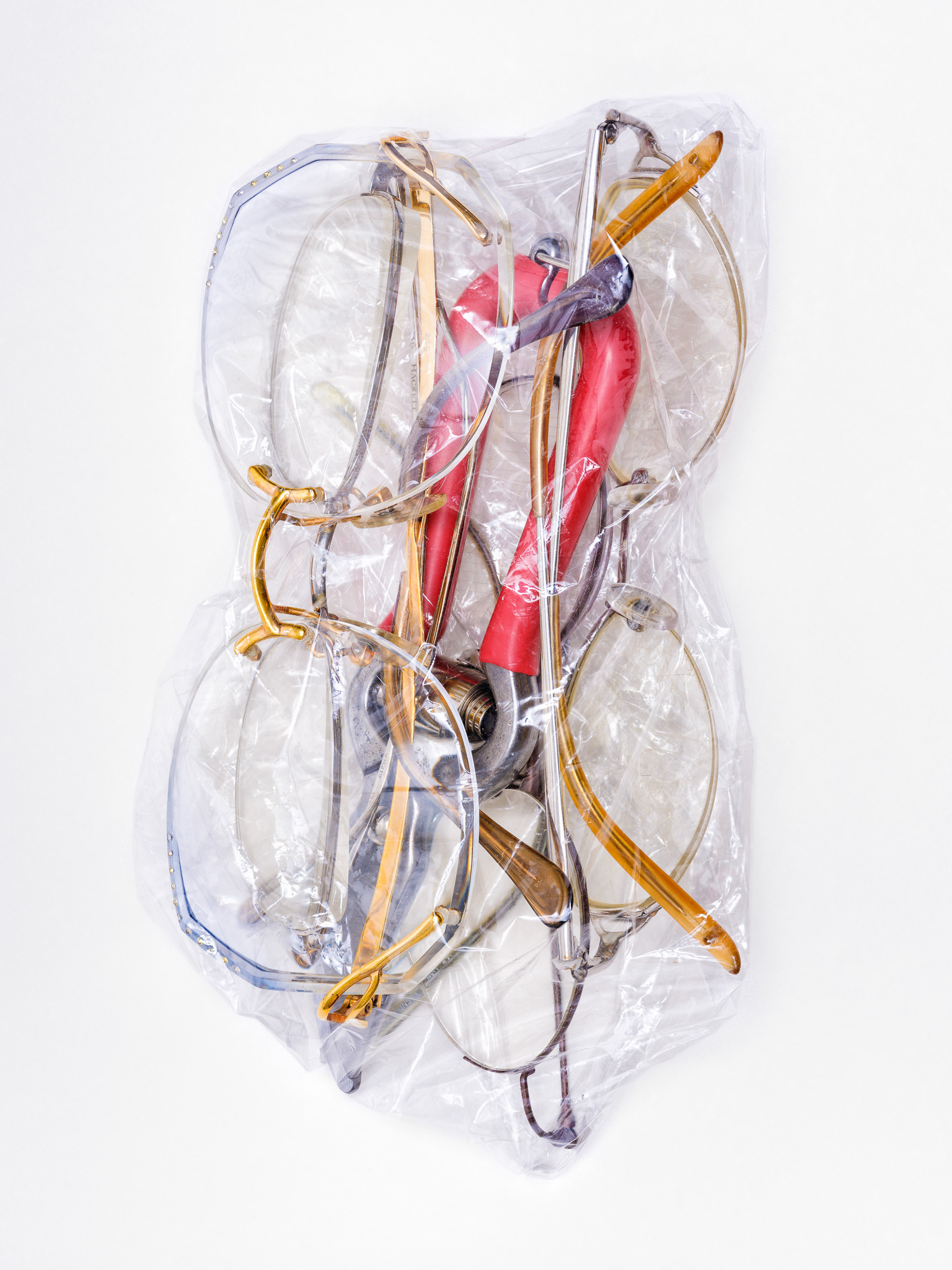 Fotografie einen Sandwiches aus Brillen und einer Gartenscheere, umwickelt von einer Lebensmittelfolie. © Piero Rossi