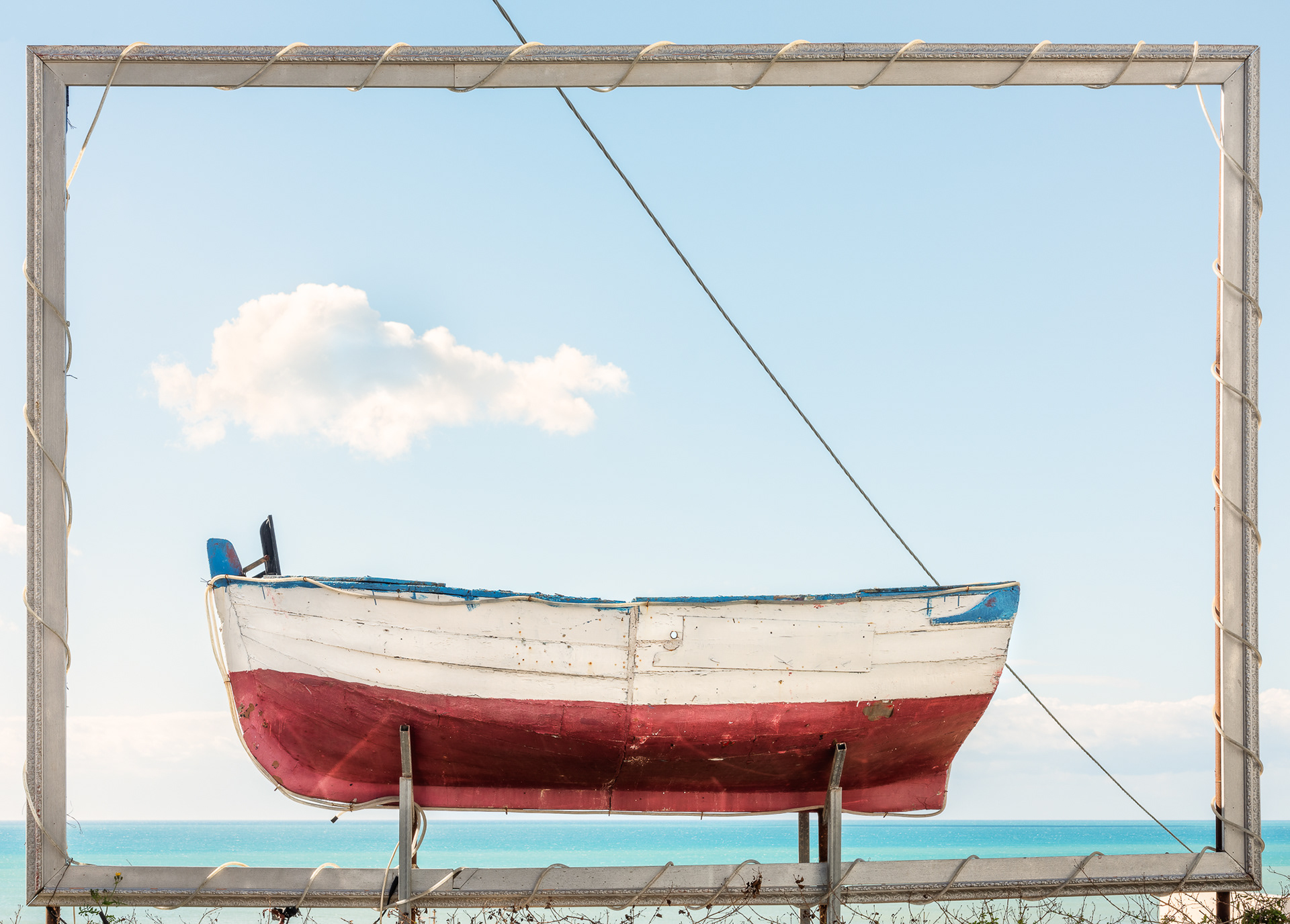 Ein grosses Boot in einem riesigen Bilderrahmen, dahinter das Meer. © Piero Rossi