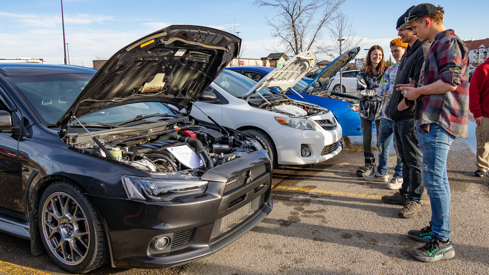 Tyler, second to right, chats with passersby who admire his modified Mitsubishi Lancer at an unofficial car meet-up in the Royal Oak Shopping Centre parking lot in NW Calgary on Sunday, April 14, 2024. Tyler claims that his car has more than 350 HP. The lot filled up with a variety of modified vehicles displayed by car enthusiasts. The fun ended at sunset when the police showed up. (Photo by Armaan Khanna/The Press)