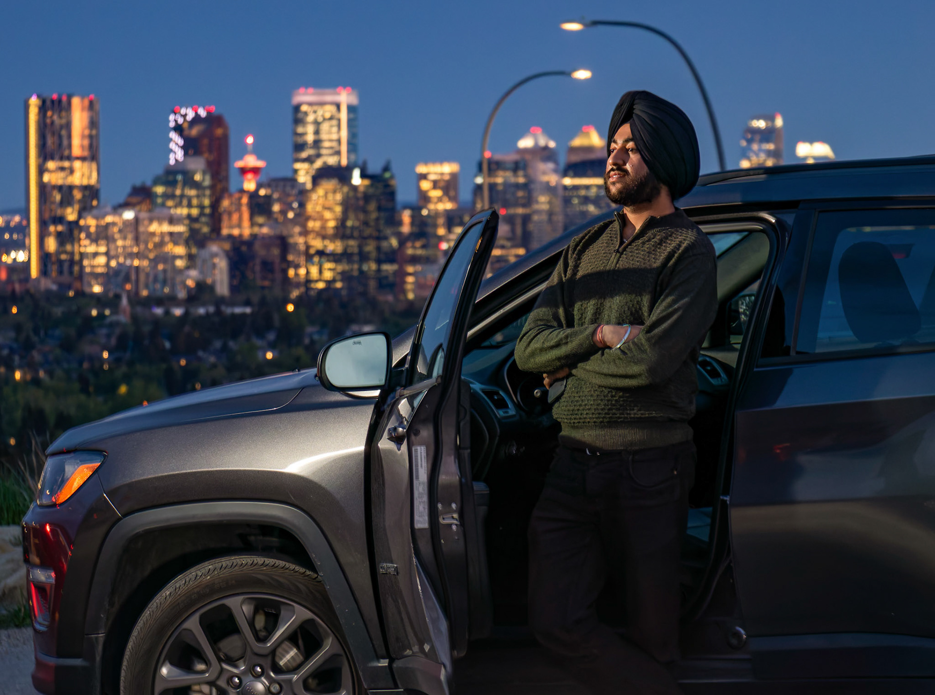 Harmandeep Singh Rathore, 20, a full-time student at SAIT studying ITS and originally from Chandigarh, India, poses for a portrait in front of his new Jeep Compass with downtown Calgary in the background on Thursday, May 30, 2024, at a viewpoint in Nose Hill Park NW Calgary. Harmandeep, who is fond of cars and loves going on long drives, dreams of becoming a successful entrepreneur and make his parents proud. (Photo by Armaan Khanna/SAIT)