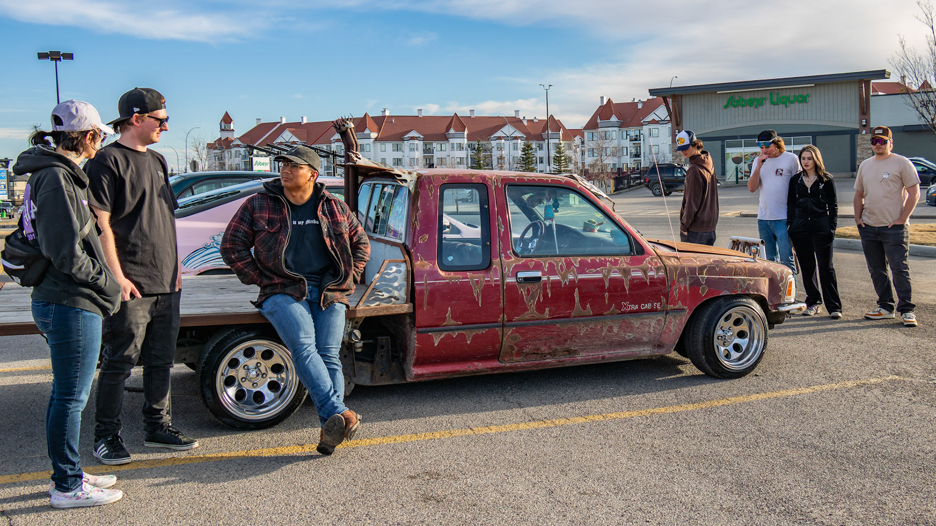 Luciana, third to left, chats with passersby who gathered to admire his modified 1999 Toyota pickup truck at an unofficial car meet-up in the Royal Oak Shopping Centre parking lot in NW Calgary on Sunday, April 14, 2024. The lot filled up with a variety of modified vehicles displayed by car enthusiasts. The fun ended at sunset when the police showed up. (Photo by Armaan Khanna/The Press)