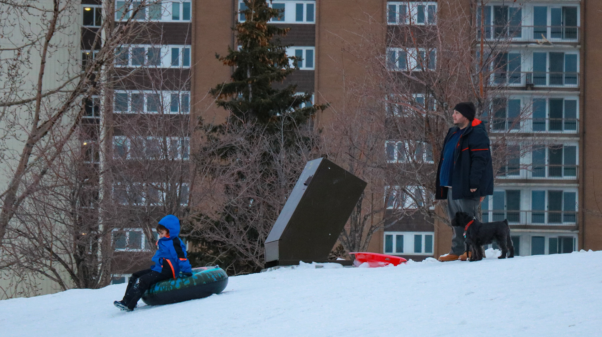 People enjoy recreational tobogganing on a city-maintained hill in Bridgeland, Calgary, on Sunday, Feb. 11, 2024. In this image, Adam is captured descending the tobogganing hill, along with the supervision of his father in the background. (Photo by Armaan Khanna/The Press)
