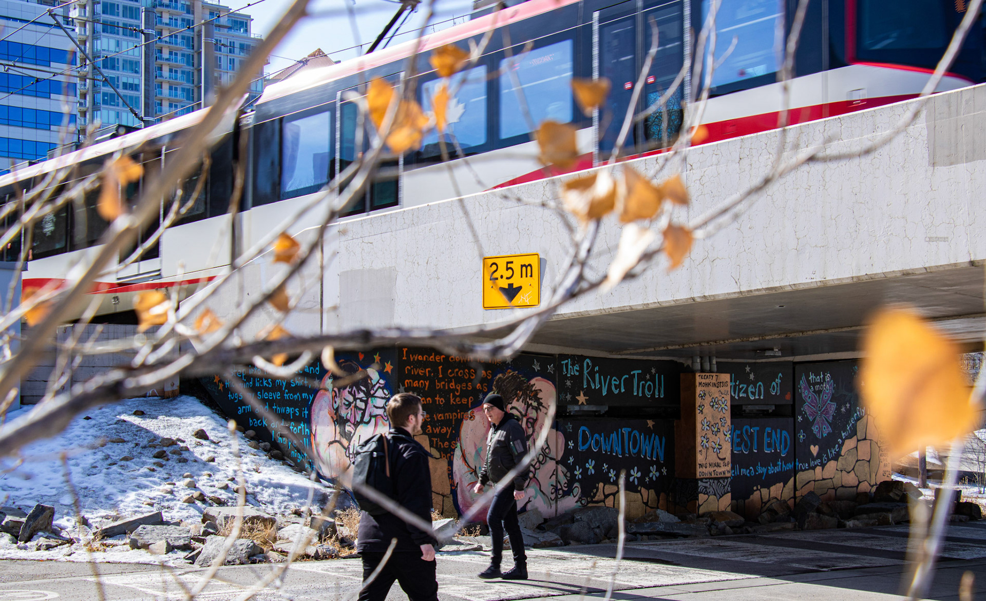 People walking along the Bow River Pathway in front of a mural painted under a C-Train bridge during a warm afternoon in Calgary on Thursday, March 14, 2024. (Photo by Armaan Khanna/The Press)