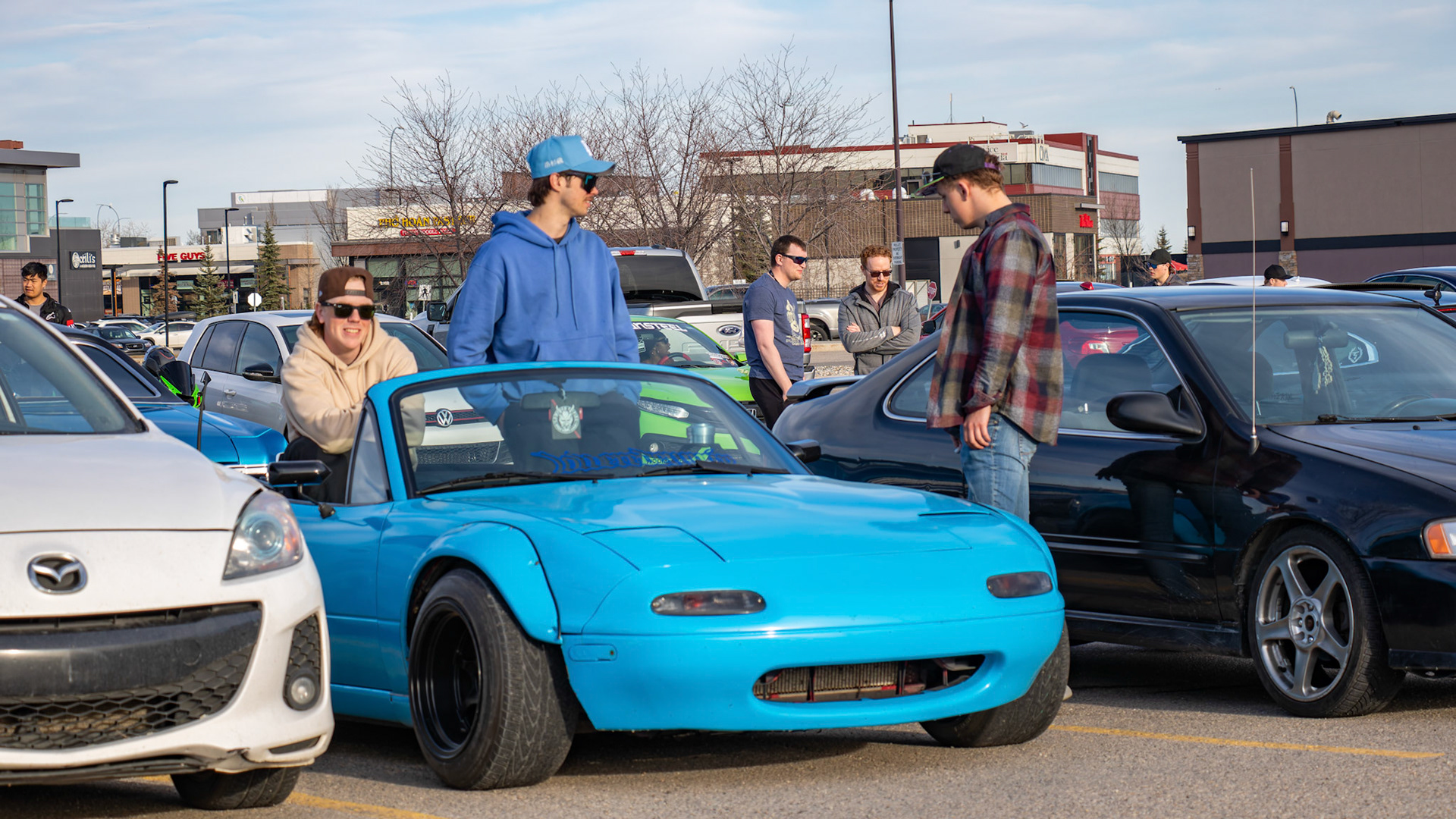 People gather to admire a modified blue Miata at an unofficial car meet-up in the Royal Oak Shopping Centre parking lot in NW Calgary on Sunday, April 14, 2024. The lot filled up with a variety of modified vehicles displayed by car enthusiasts. The fun ended at sunset when the police showed up. (Photo by Armaan Khanna/The Press)