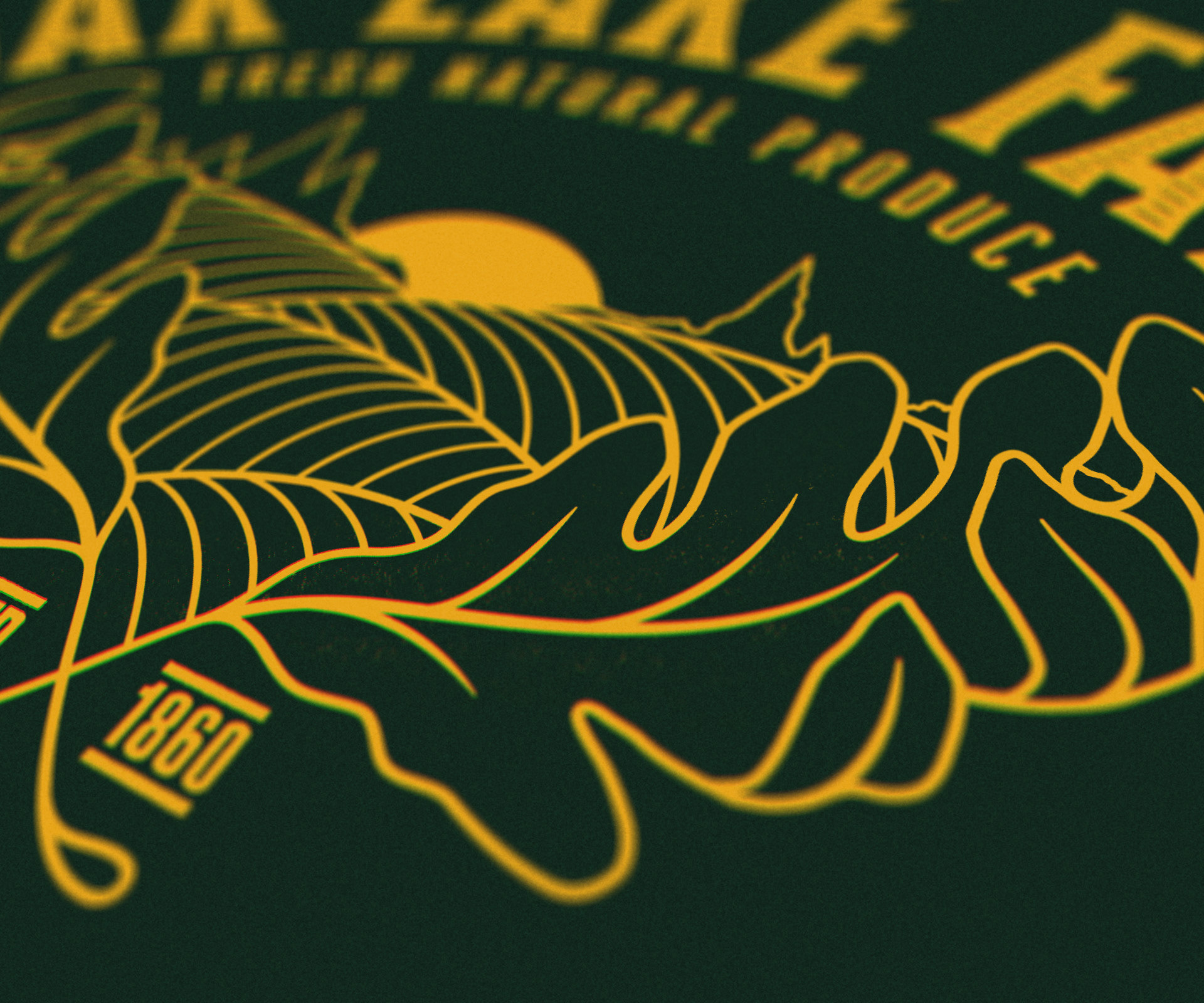 A close-up macro view of the secondary logo for Oak Lake Farm, with warm yellow text and sunset hill illustration, on a dark green background.