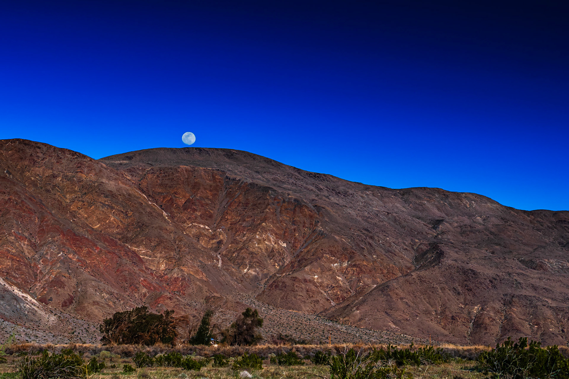 Evening Moonrise: Viewed across the creosote-bush studded, alluvial plain near the entrance to Coyote Canyon in the Anza-Borrego Desert.  A house nestled in a copse of willows sites at the far side of the plain at the foot of the mountain.