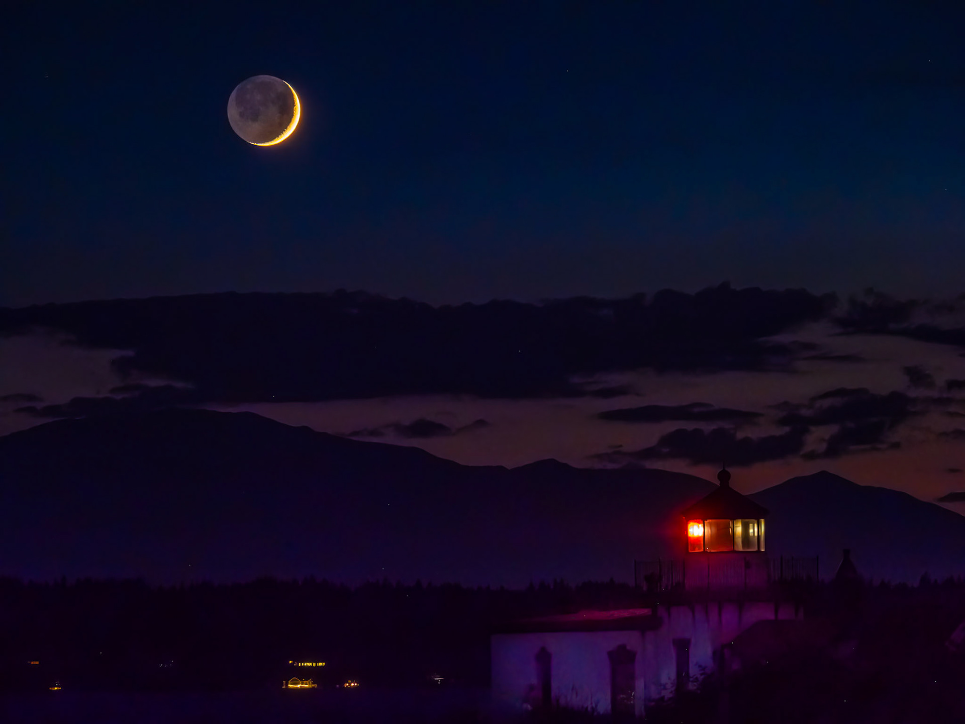 Crescent Moon Setting: A setting crescent moon  provides faint illumination to the Kitsap Peninsula in the background while the West Point Lghthouse at Seattle's Discovery Park flashes its beacon to vessels in the Puget Sound in the foreground.